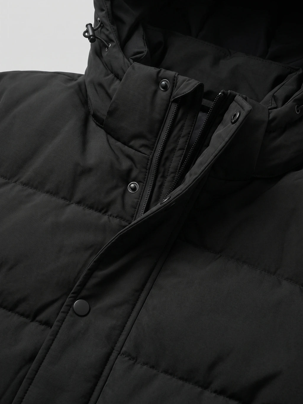 Close-up of the Black Hooded Puffer Jacket showing the front zipper, snap-button storm flap, and adjustable hood drawcord.