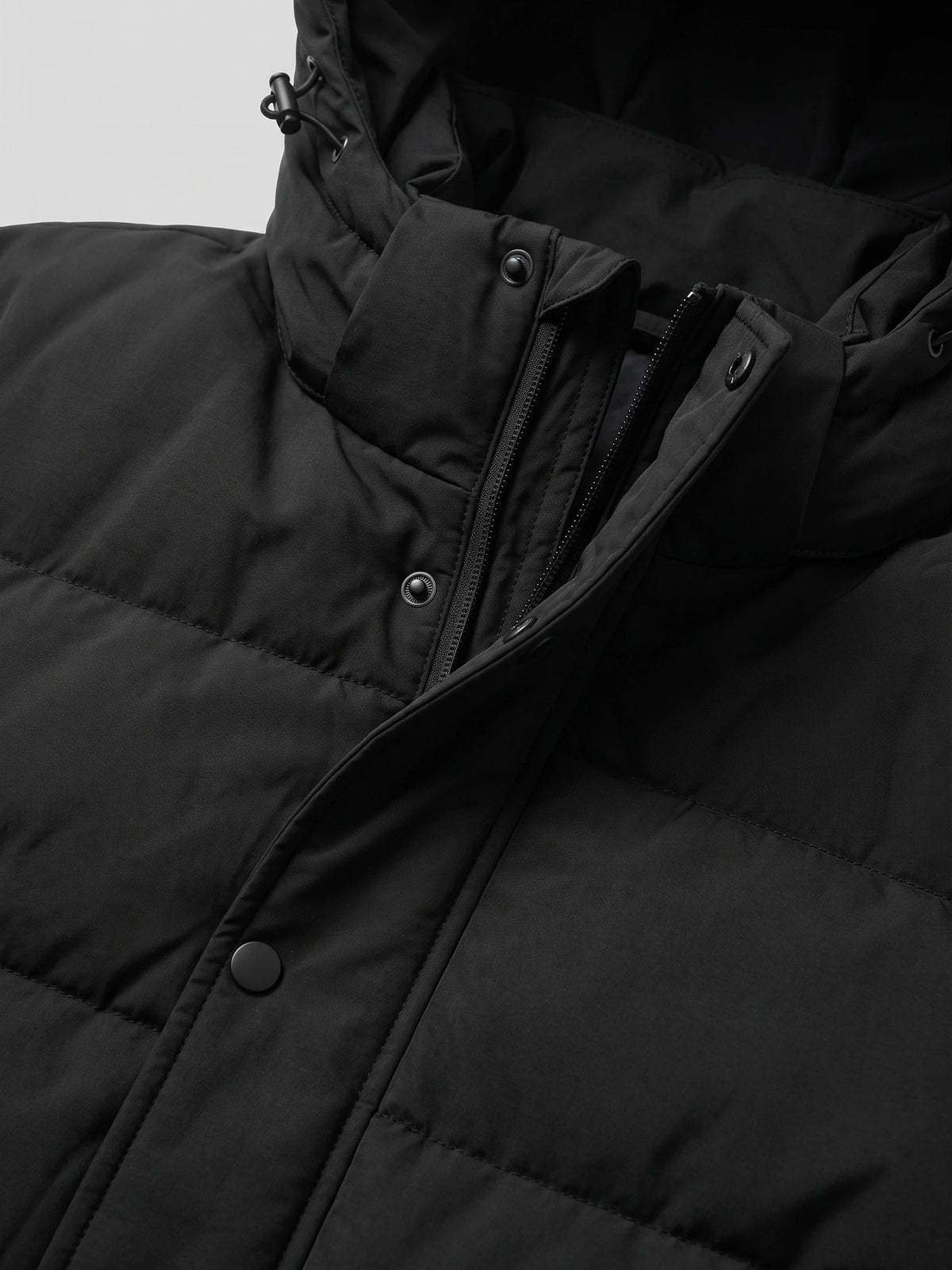 Close-up of the Black Hooded Puffer Jacket showing the front zipper, snap-button storm flap, and adjustable hood drawcord.