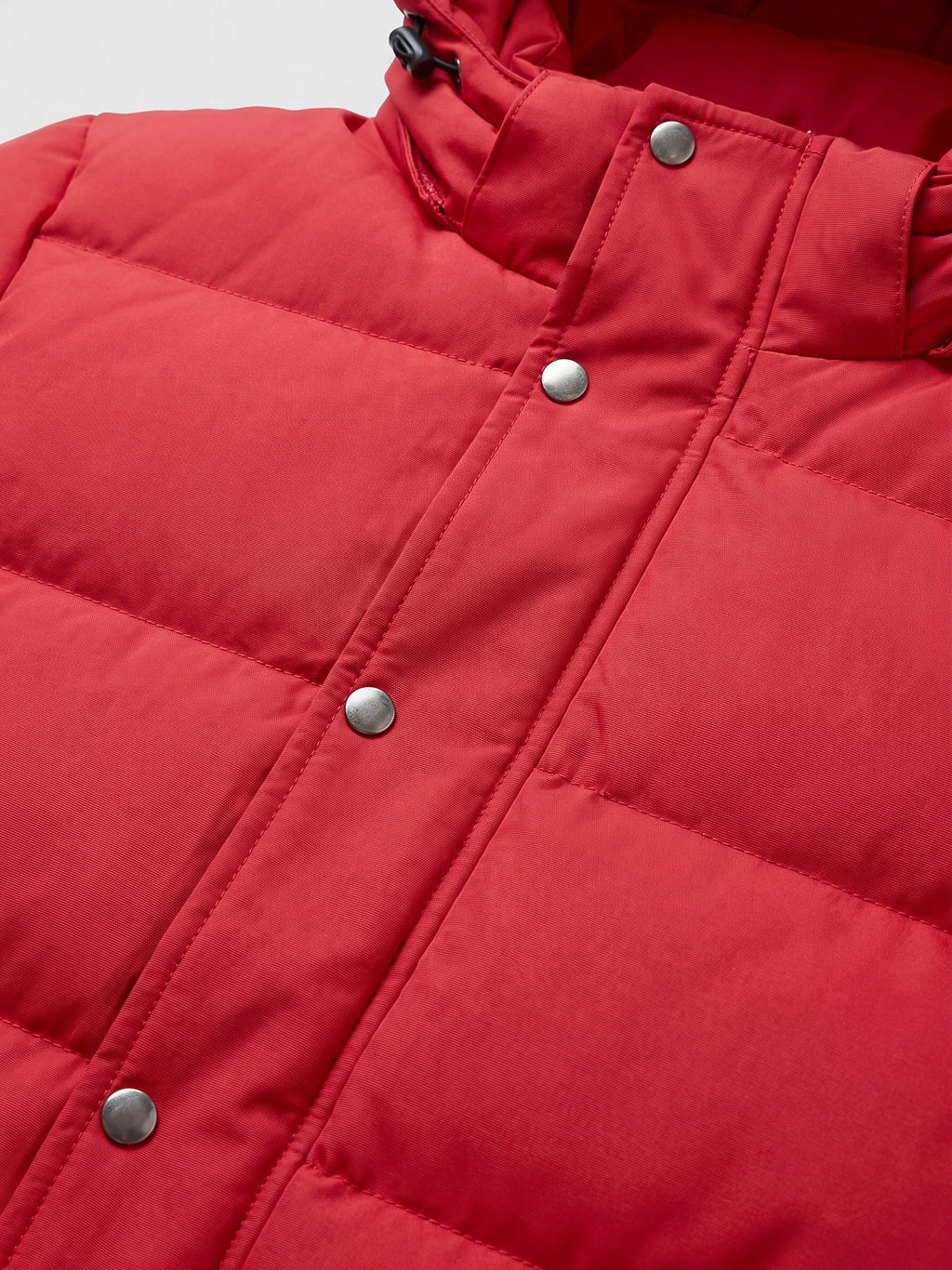 Red hooded puffer jacket close-up showing quilted stitching, snap-button storm flap, and adjustable hood drawcord.