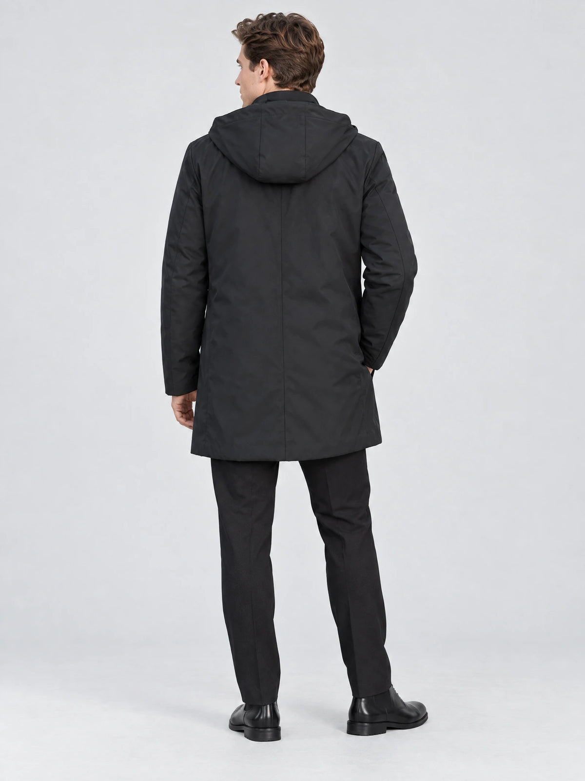 Rear studio view of a model wearing a Black men’s hooded trench coat with a center back seam.