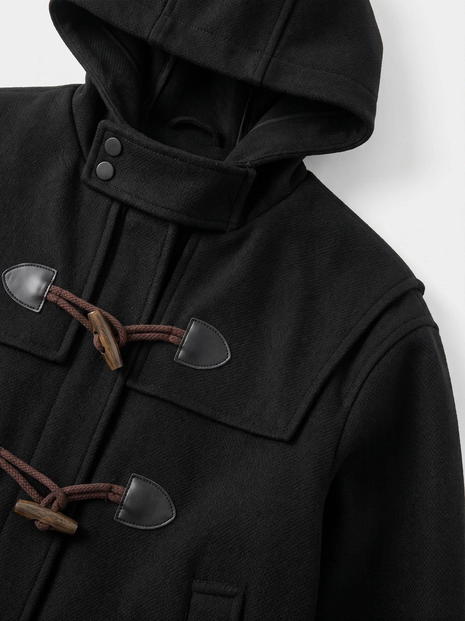 Close-up of the Black wool men’s trench coat hood, snap-tab collar, and toggle fastenings.