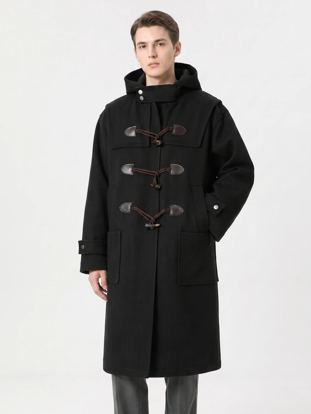 Front studio view of a model wearing a Black wool hooded trench coat with toggle fastenings and patch pockets.