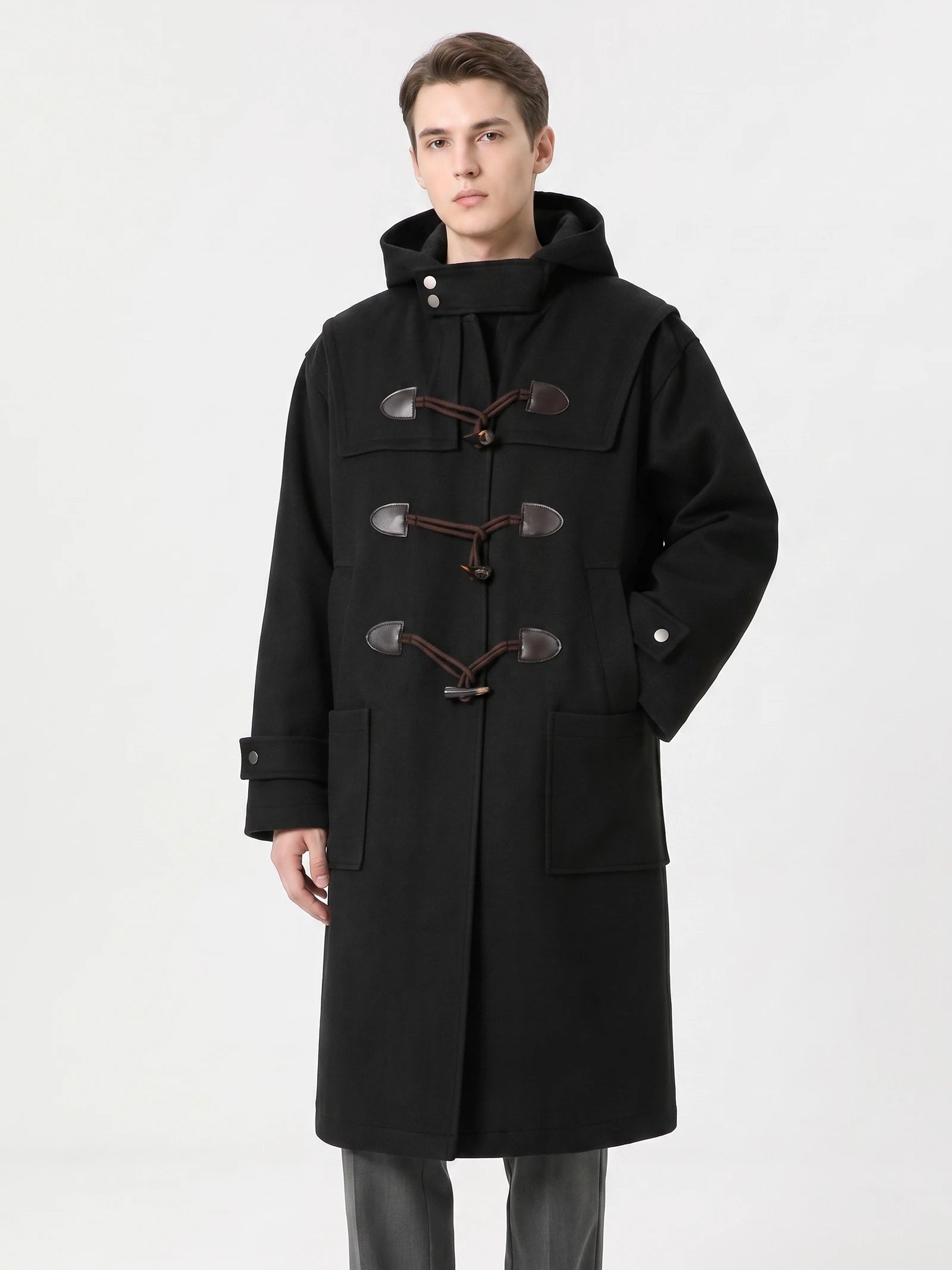 Front studio view of a model wearing a Black wool hooded trench coat with toggle fastenings and patch pockets.