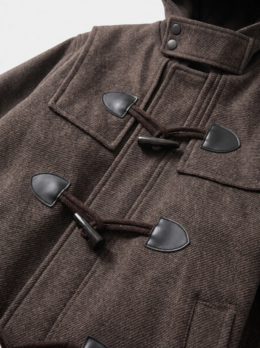 Close-up of the Brown wool trench coat’s textured fabric, toggle closures, and stand collar with snap buttons.