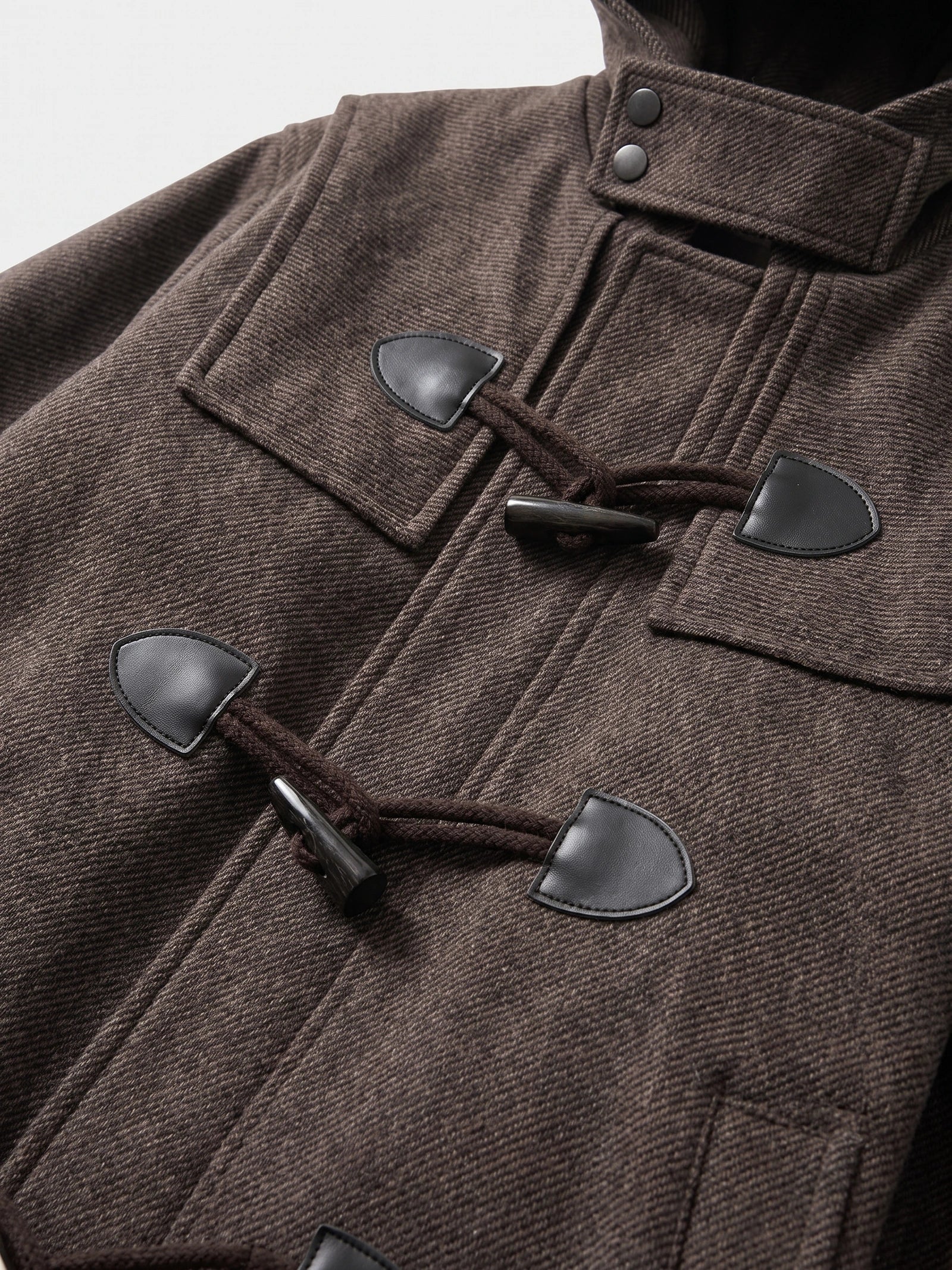 Close-up of the Brown wool trench coat’s textured fabric, toggle closures, and stand collar with snap buttons.