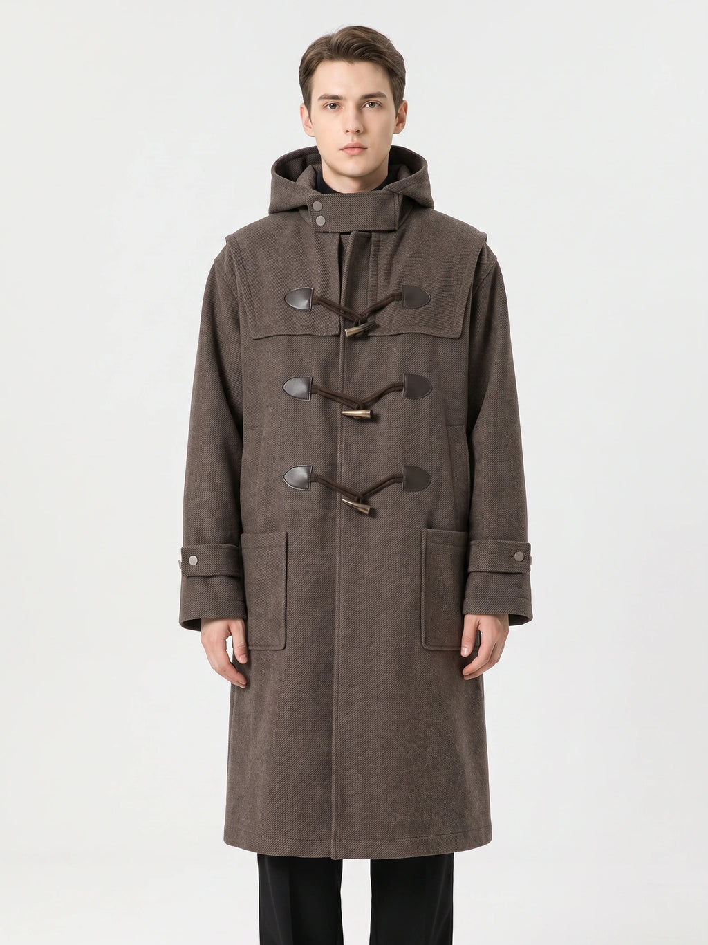 Front studio view of a model wearing a Brown wool trench coat with a hood, toggle fastenings, cuff tabs, and flap pockets.