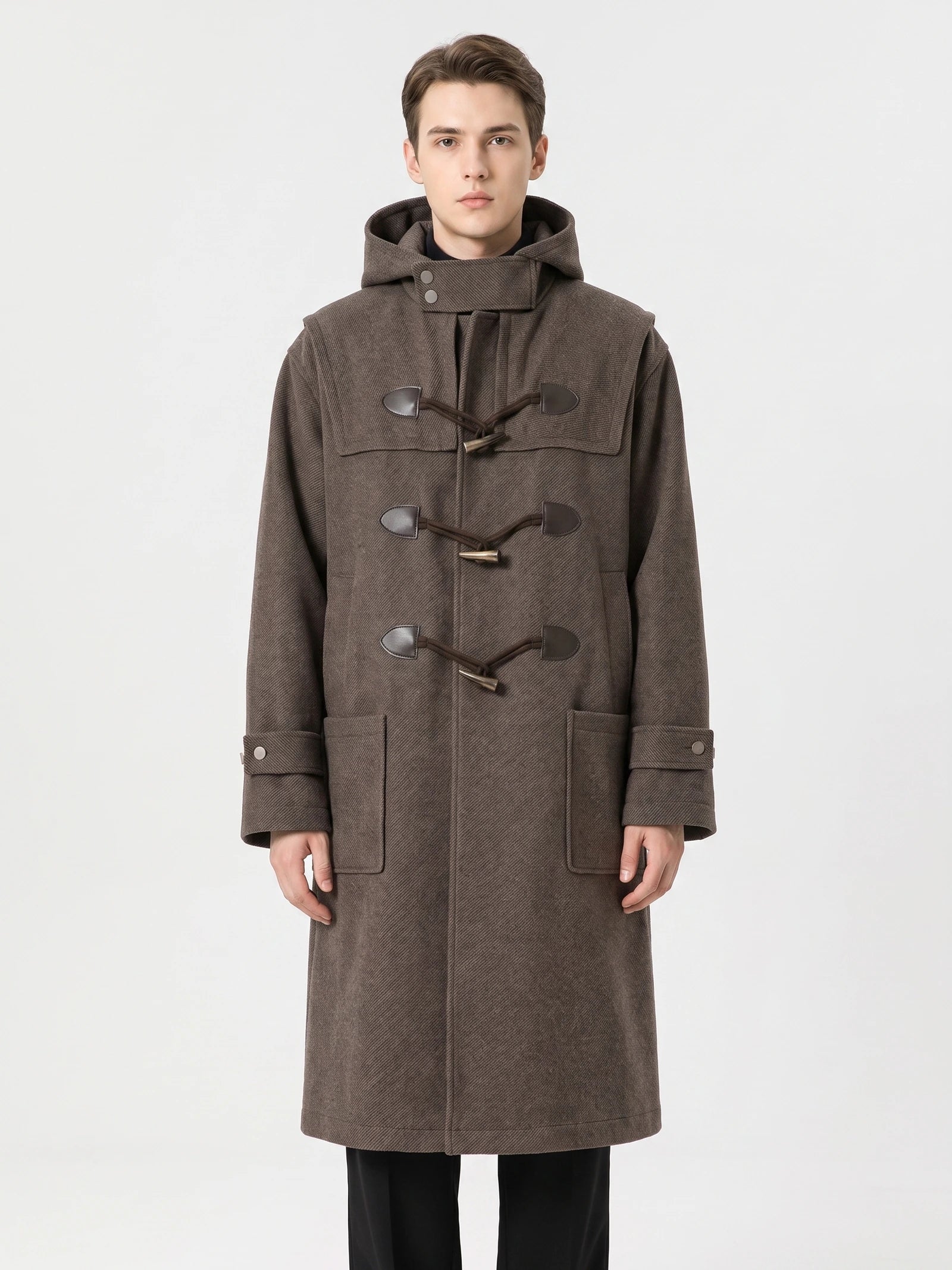 Front studio view of a model wearing a Brown wool trench coat with a hood, toggle fastenings, cuff tabs, and flap pockets.