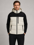 Front view of a man wearing a beige hooded puffer vest with a windproof shell, thick insulation, sleeveless design, and full zip front