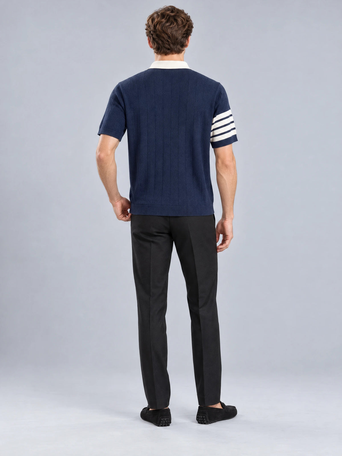 Rear studio view of a model wearing a Navy Knit Polo with a ribbed hem and striped short-sleeve cuff.