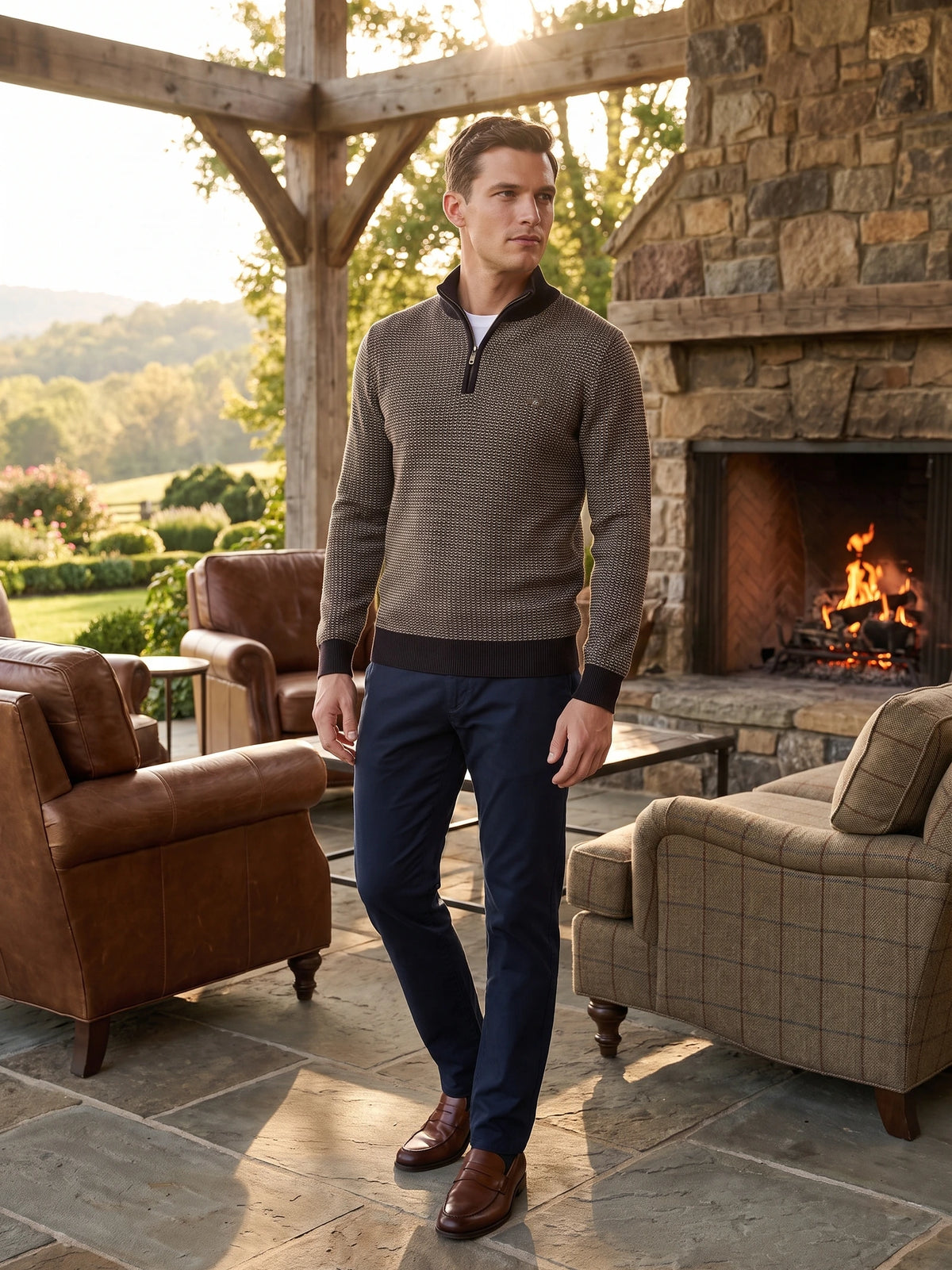Man wearing a Brown knit quarter zip sweater on a sunlit patio beside a stone fireplace.