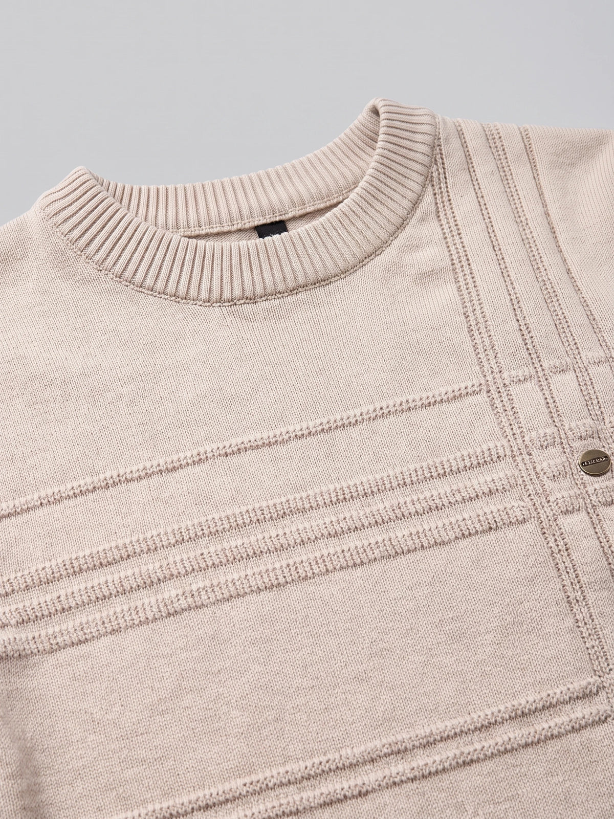 Close-up of a Beige knitted cotton sweater with a ribbed crewneck and textured geometric knit pattern.