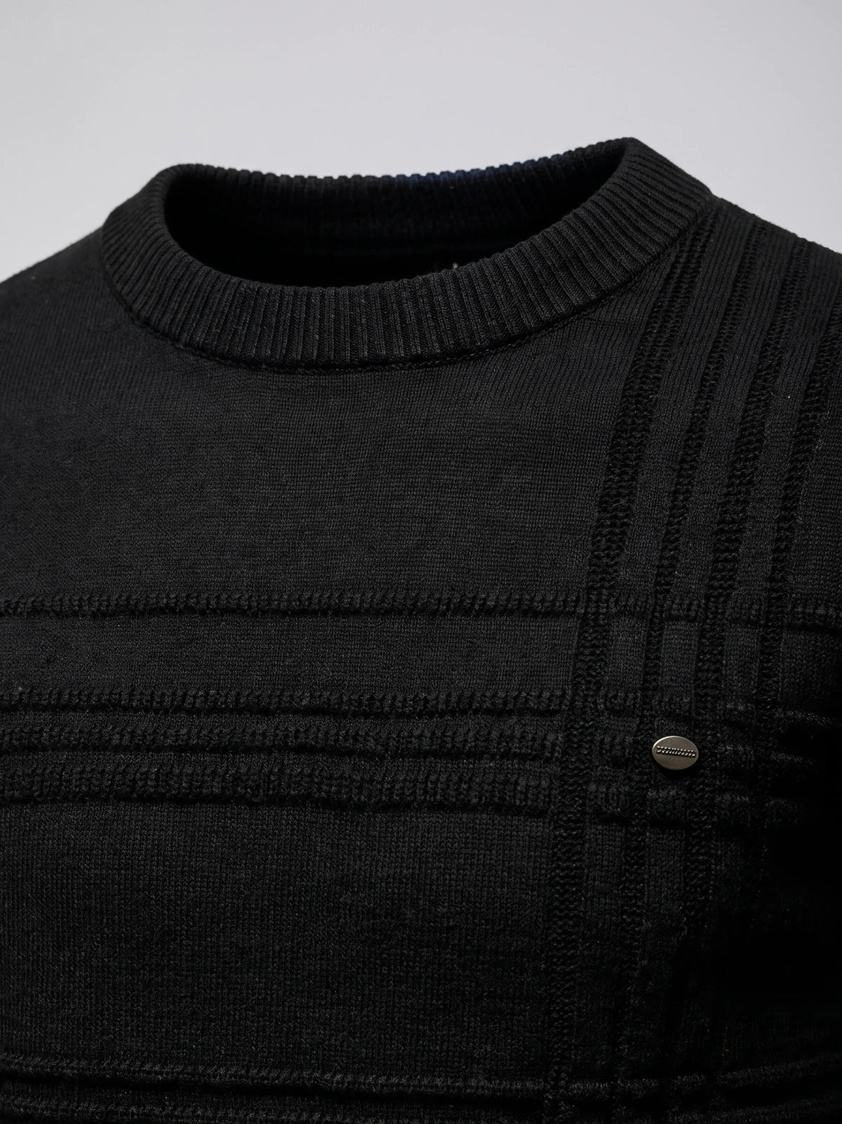 Close-up of the Black knitted cotton sweater’s ribbed crewneck, textured knit panels, and chest button detail.