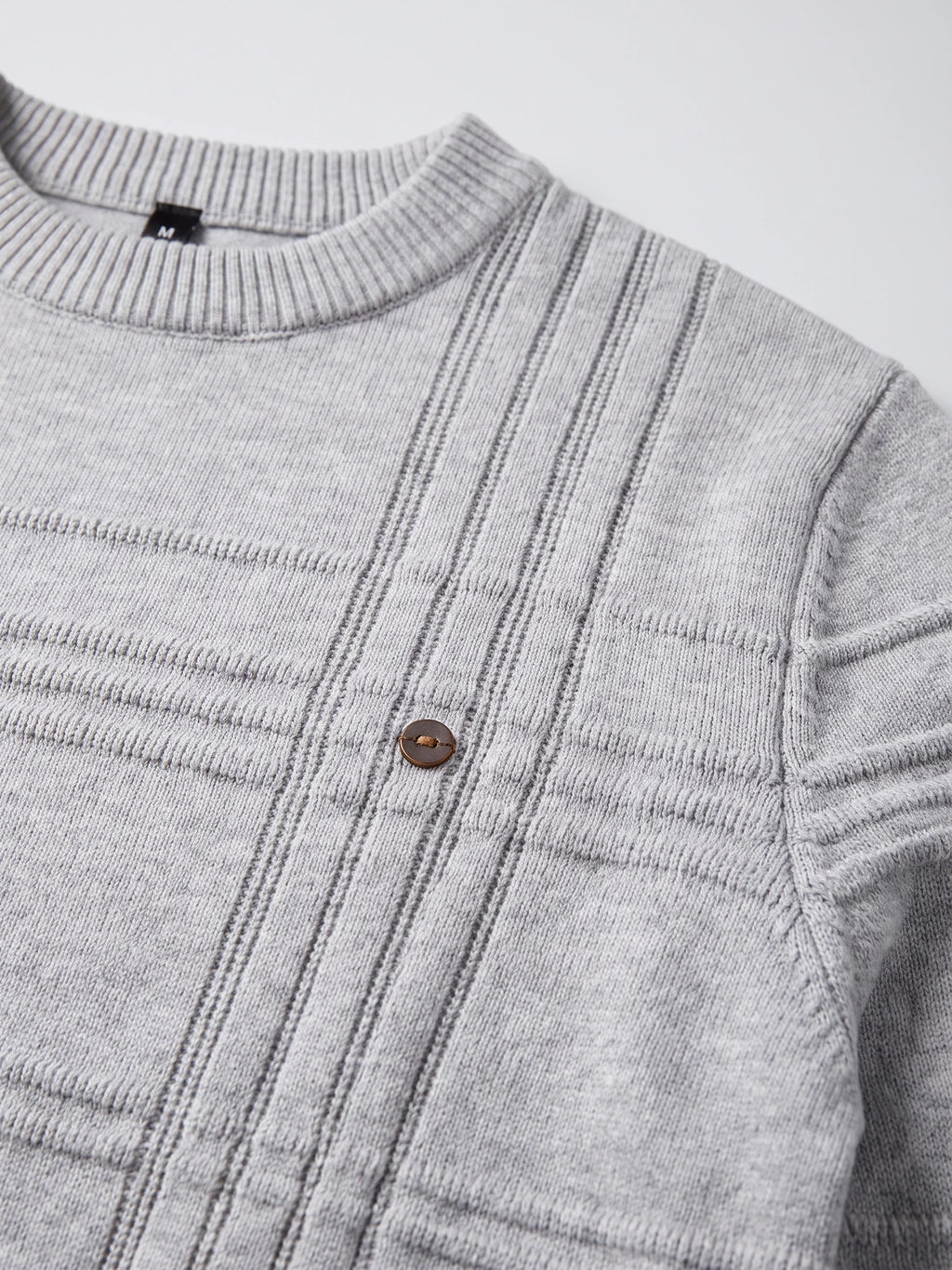 Close-up of the Gray knitted cotton sweater showing its ribbed crewneck, textured vertical knit pattern, shoulder seam, and button detail.