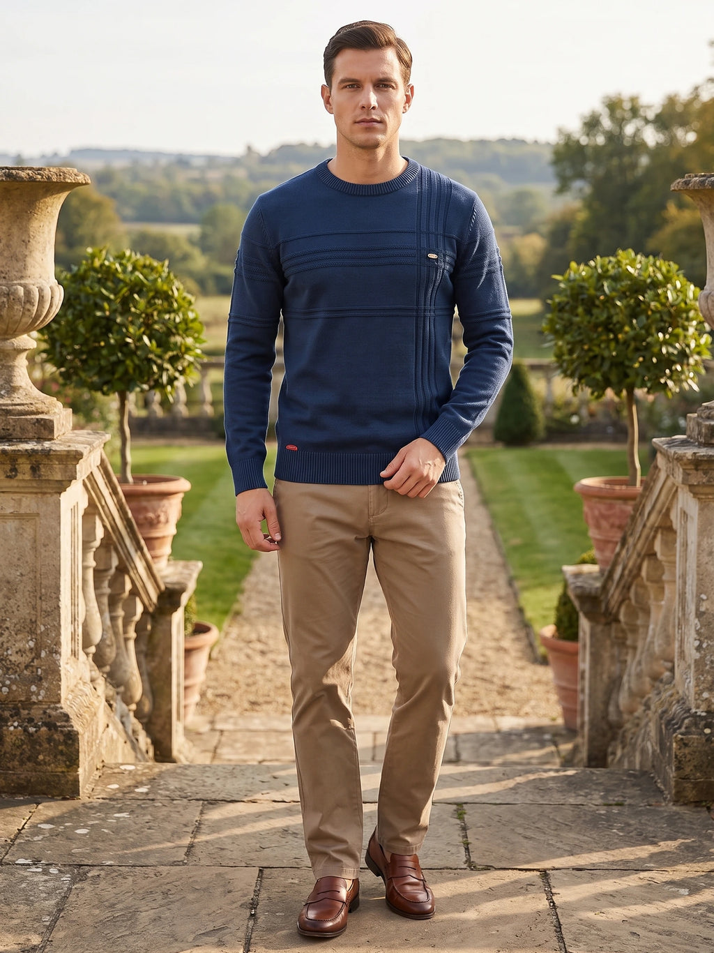 Model wearing a Navy knitted cotton crewneck sweater with textured front panels while walking along a garden terrace.