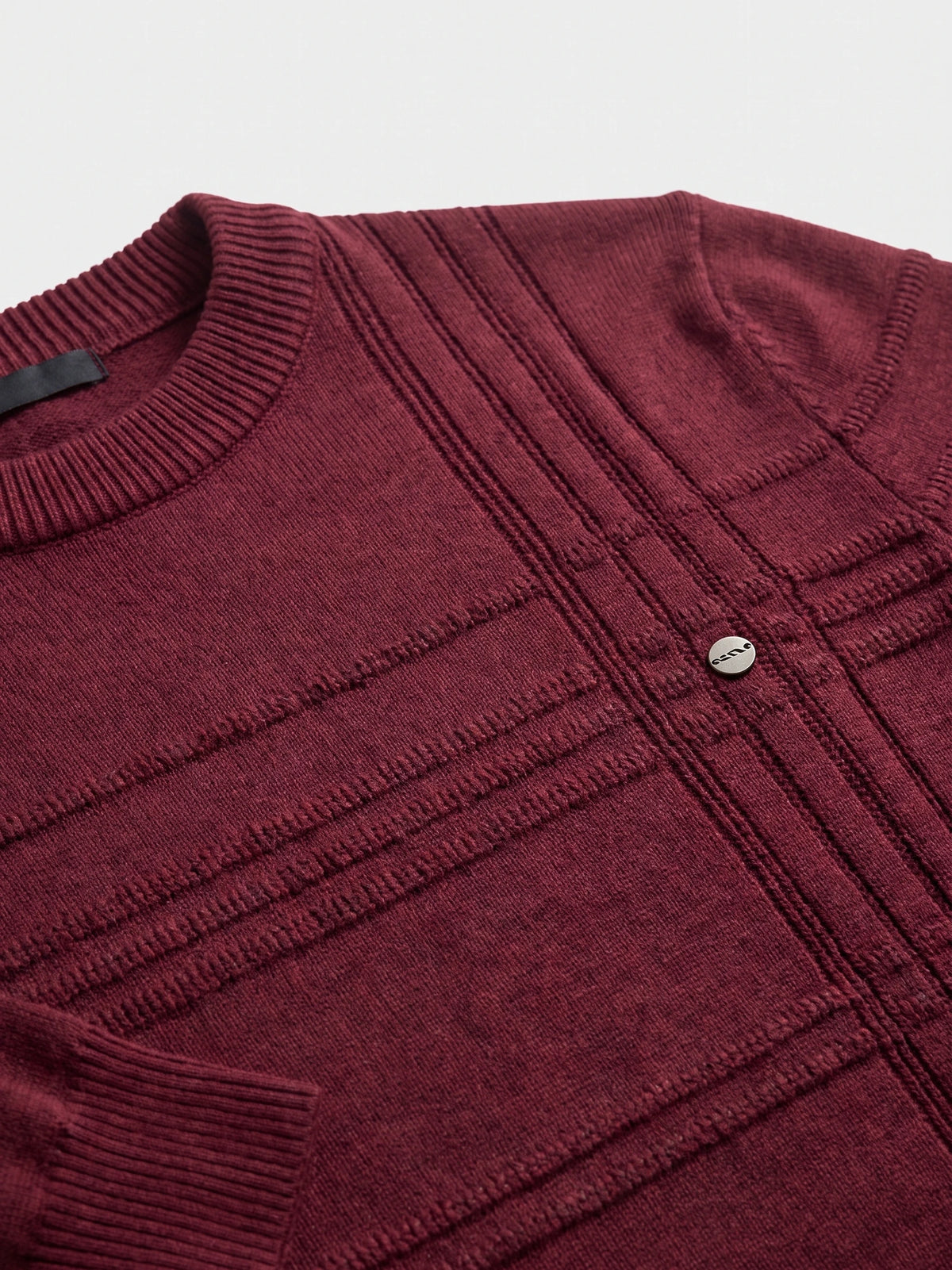 Close-up of the Wine knitted cotton sweater showing its ribbed crewneck, textured knit panels, and small chest emblem.