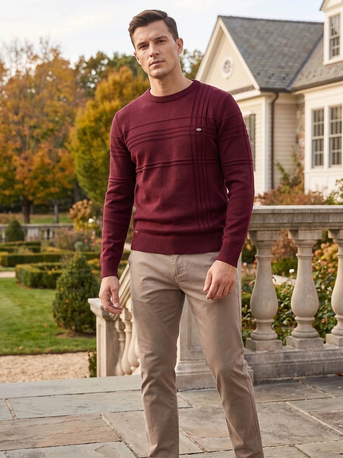 Model wearing a Wine knitted cotton crewneck sweater with textured chest panels outside a house.