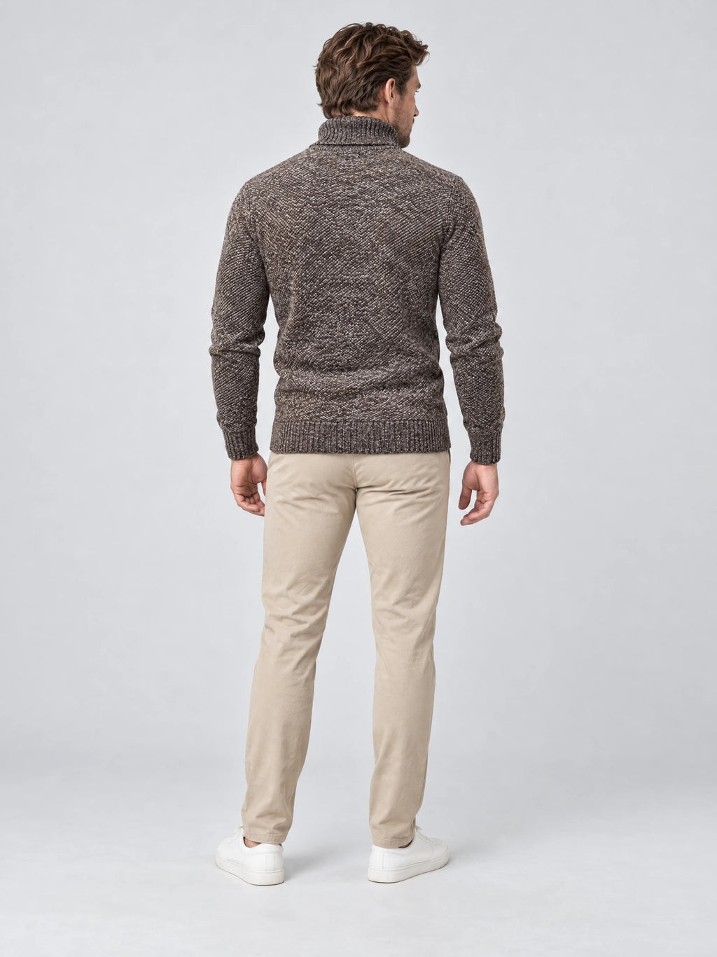 Rear studio view of a model wearing a Brown knitted turtleneck sweater with ribbed cuffs and hem.