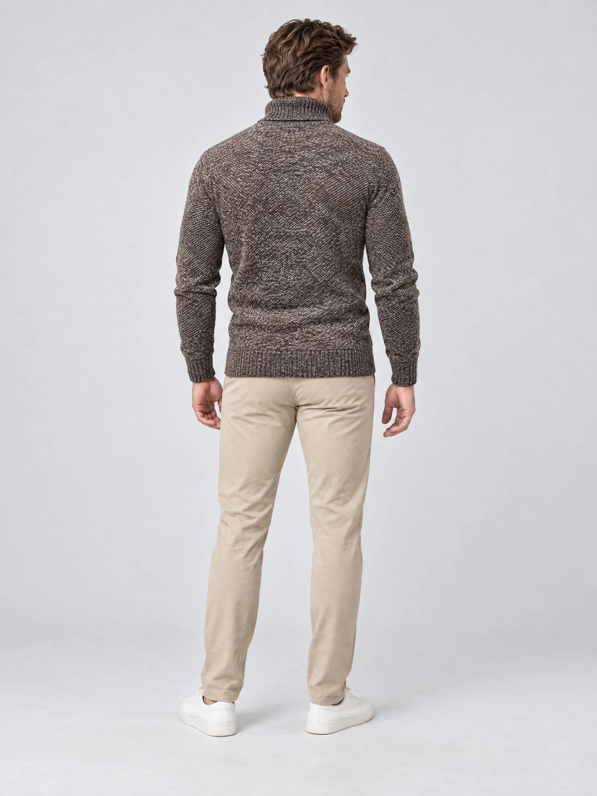Rear studio view of a model wearing a Brown knitted turtleneck sweater with ribbed cuffs and hem.