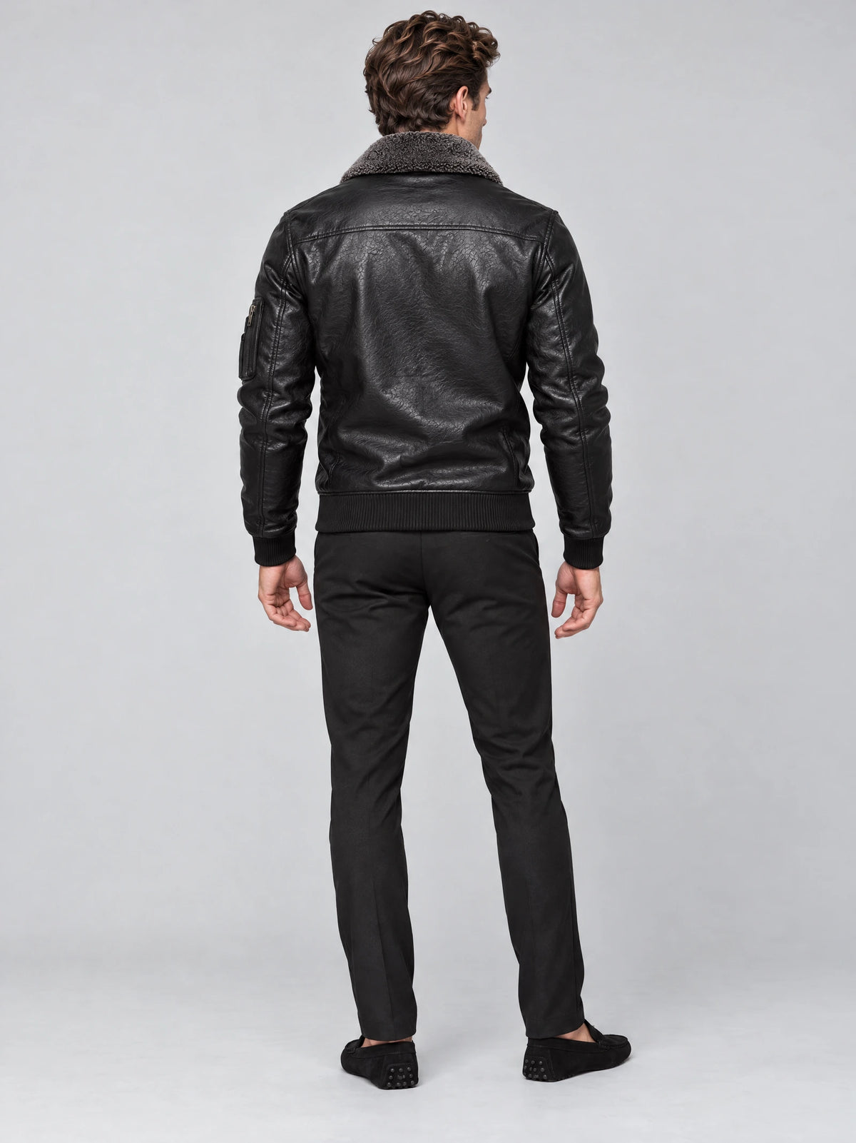 Rear studio view of a model wearing a Black Leather Aviator Jacket with a textured collar, back yoke seam, and ribbed hem and cuffs.