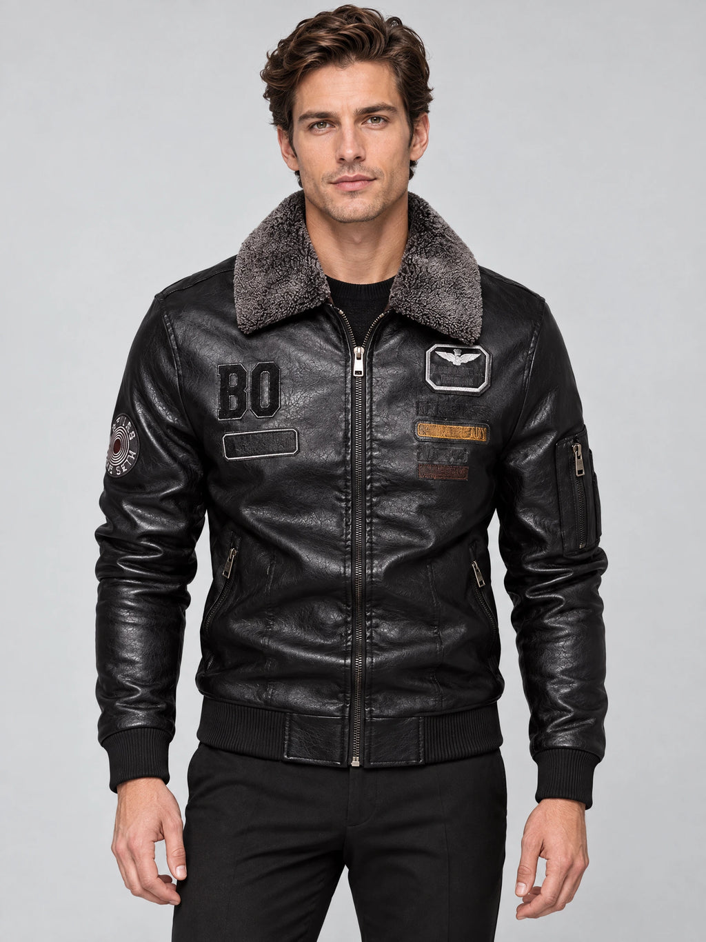 Front studio view of a model wearing a Black Leather Aviator Jacket with a fur collar, zip front, ribbed trim, and chest patches.