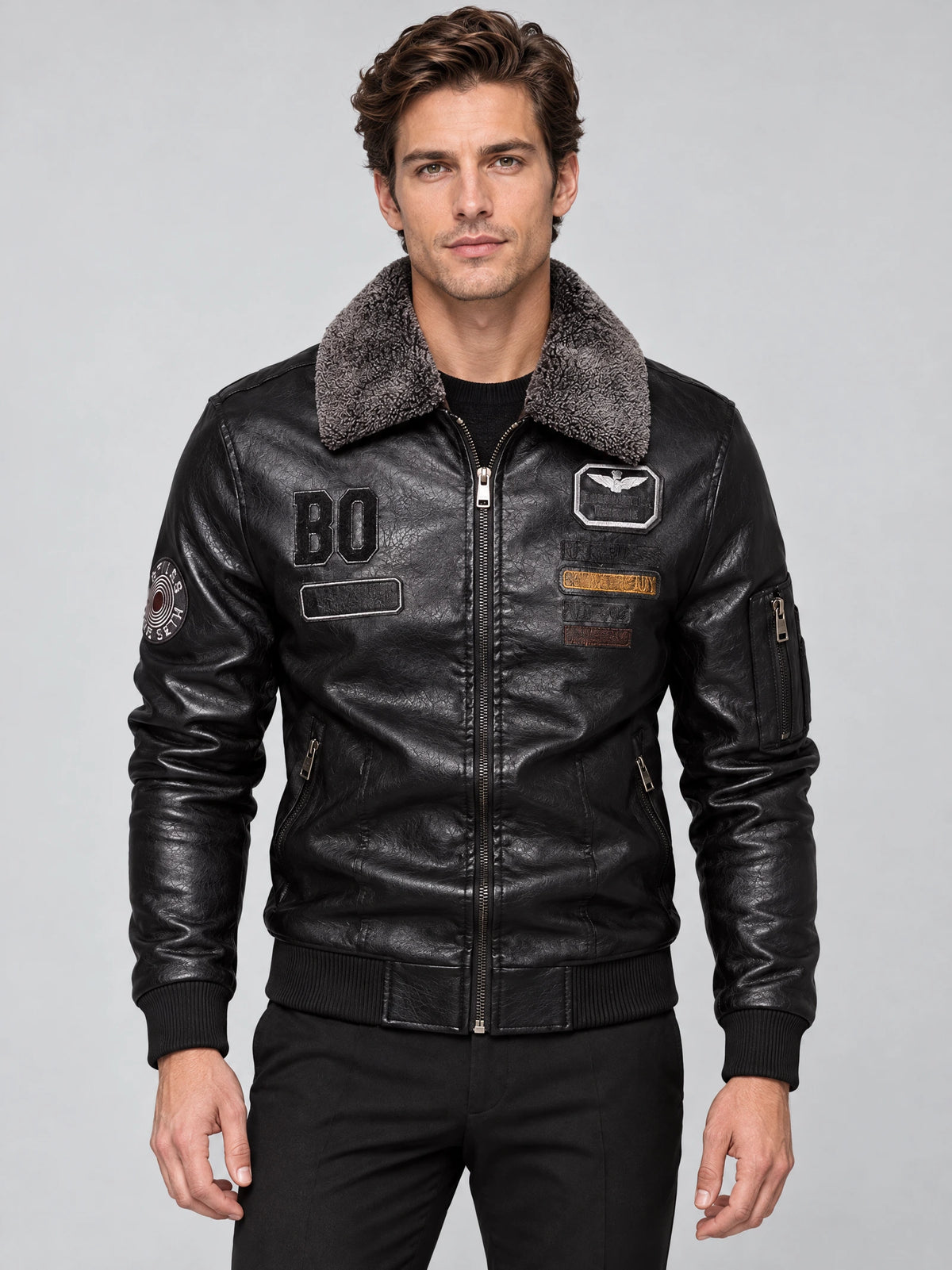 Front studio view of a model wearing a Black Leather Aviator Jacket with a fur collar, zip front, ribbed trim, and chest patches.