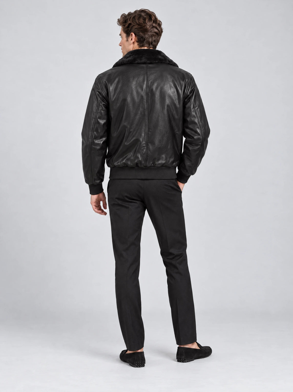 Rear studio view of a model wearing a Black leather bomber jacket with a plush collar, back seam, and ribbed hem.