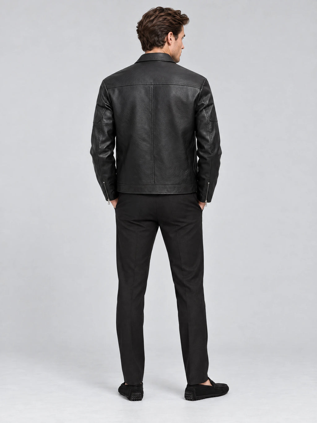 Rear studio view of a model wearing a Black leather bomber jacket with a back yoke, center seam, and zippered cuffs.