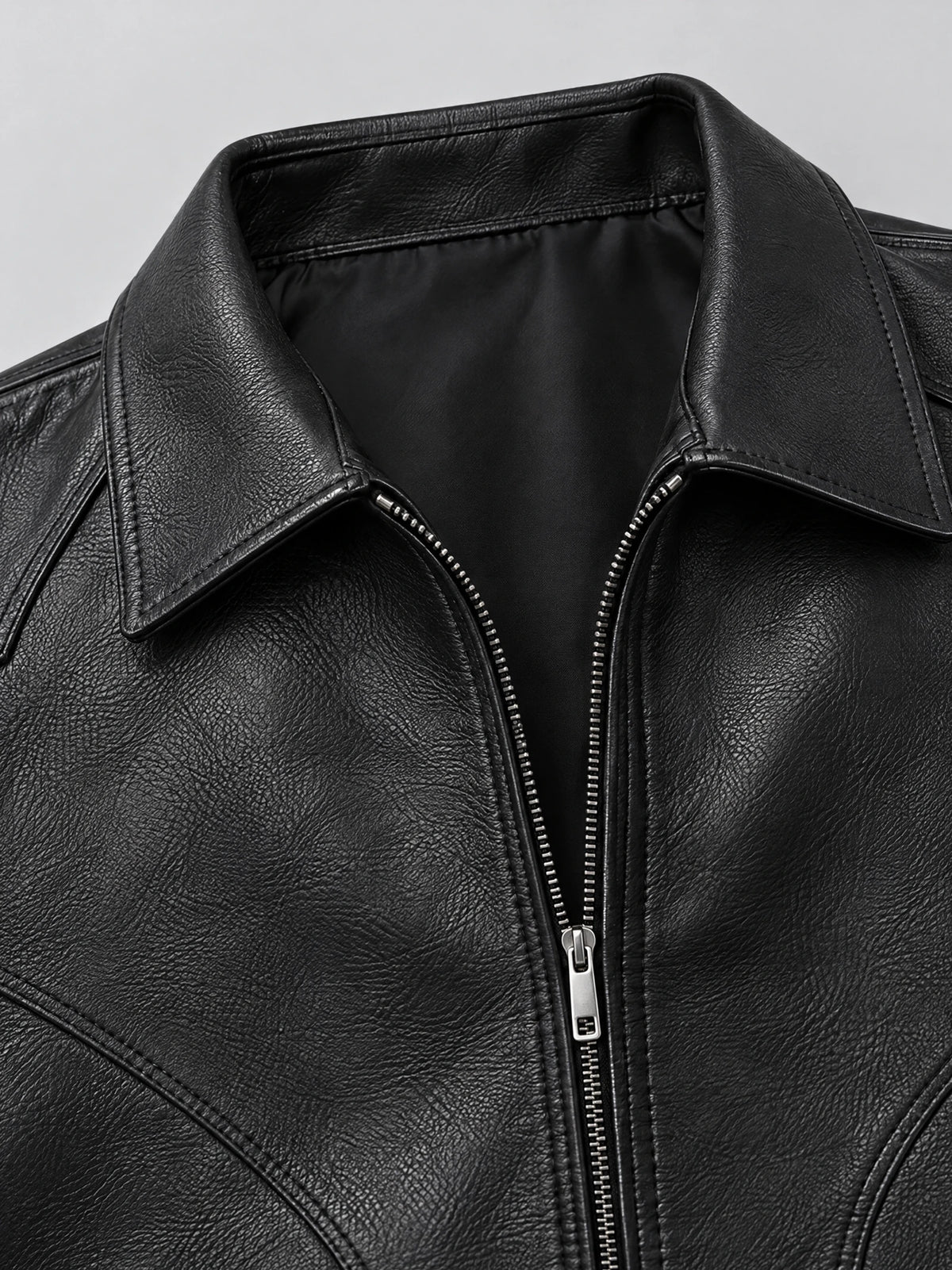 Close-up of the Black leather bomber jacket showing its textured PU leather, pointed collar, and front zipper.