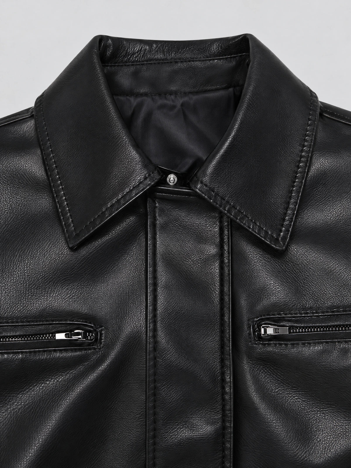 Close-up of the Black leather bomber jacket's lapel collar, textured finish, snap tab, and zippered chest pockets.