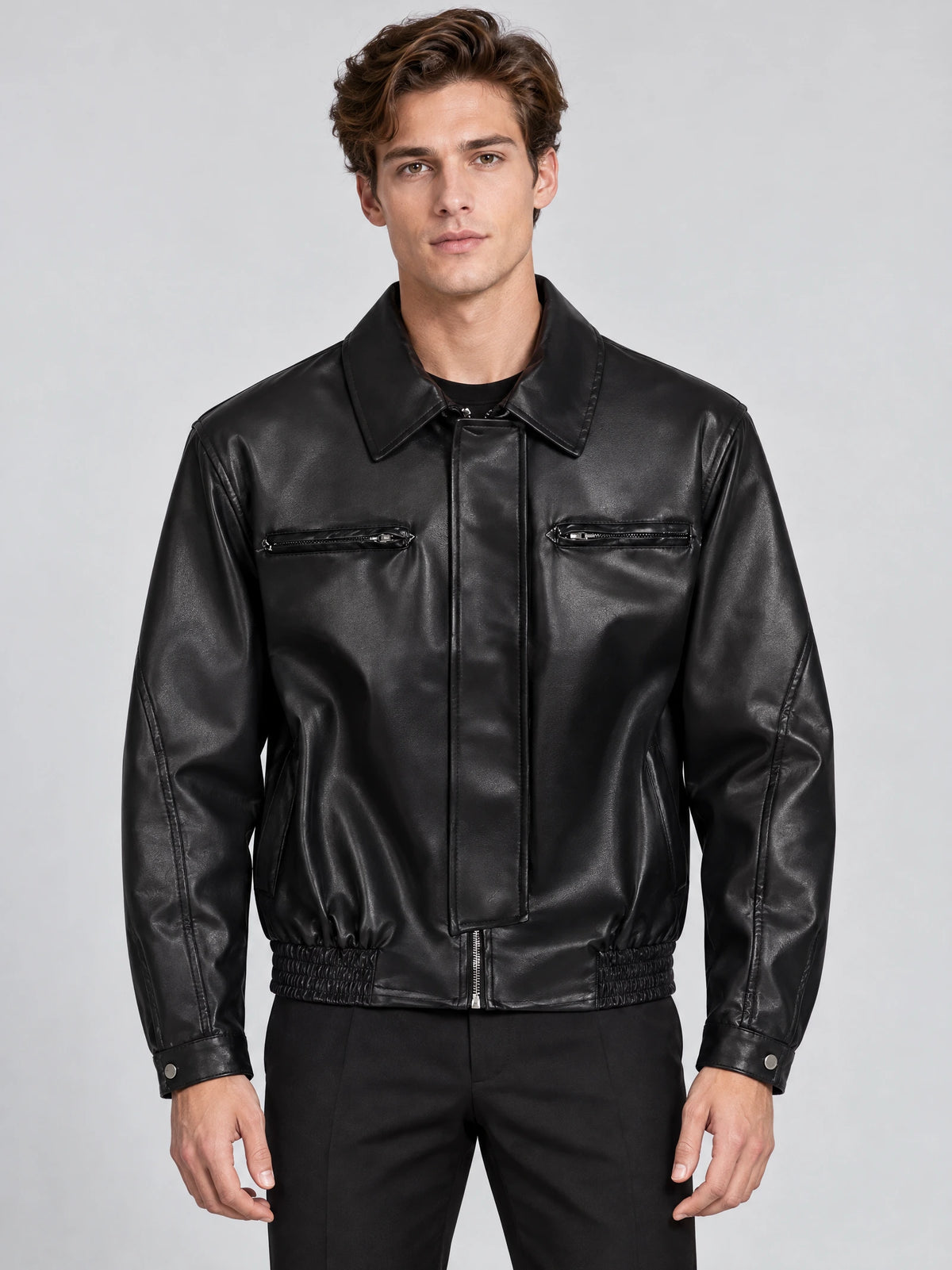 Front studio view of a model wearing a Black leather bomber jacket with a lapel collar, zip chest pockets, and elasticated hem.
