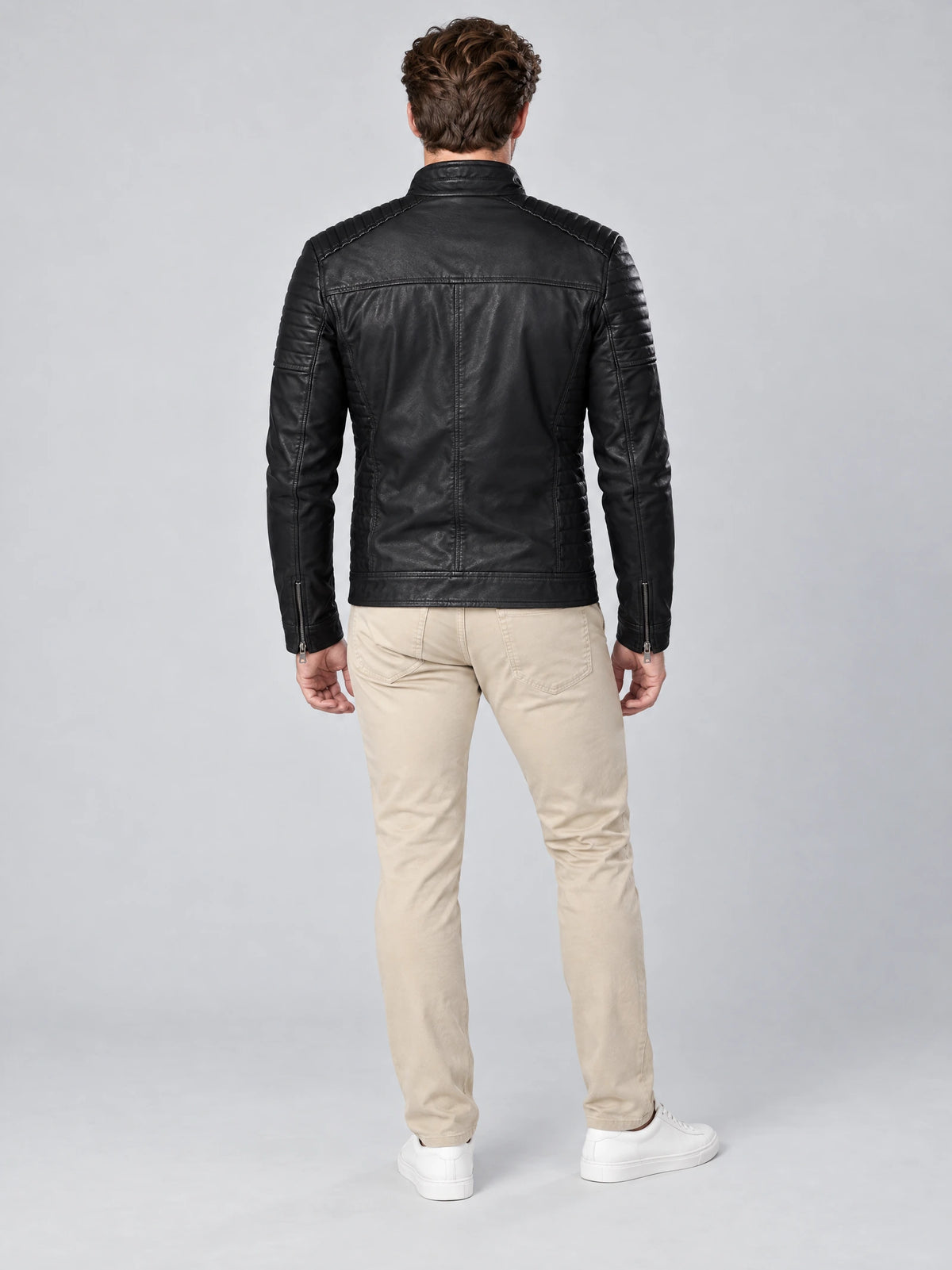 Rear studio view of a model wearing a Black Leather Fall Jacket with quilted shoulder panels, back seams, and zip cuffs.