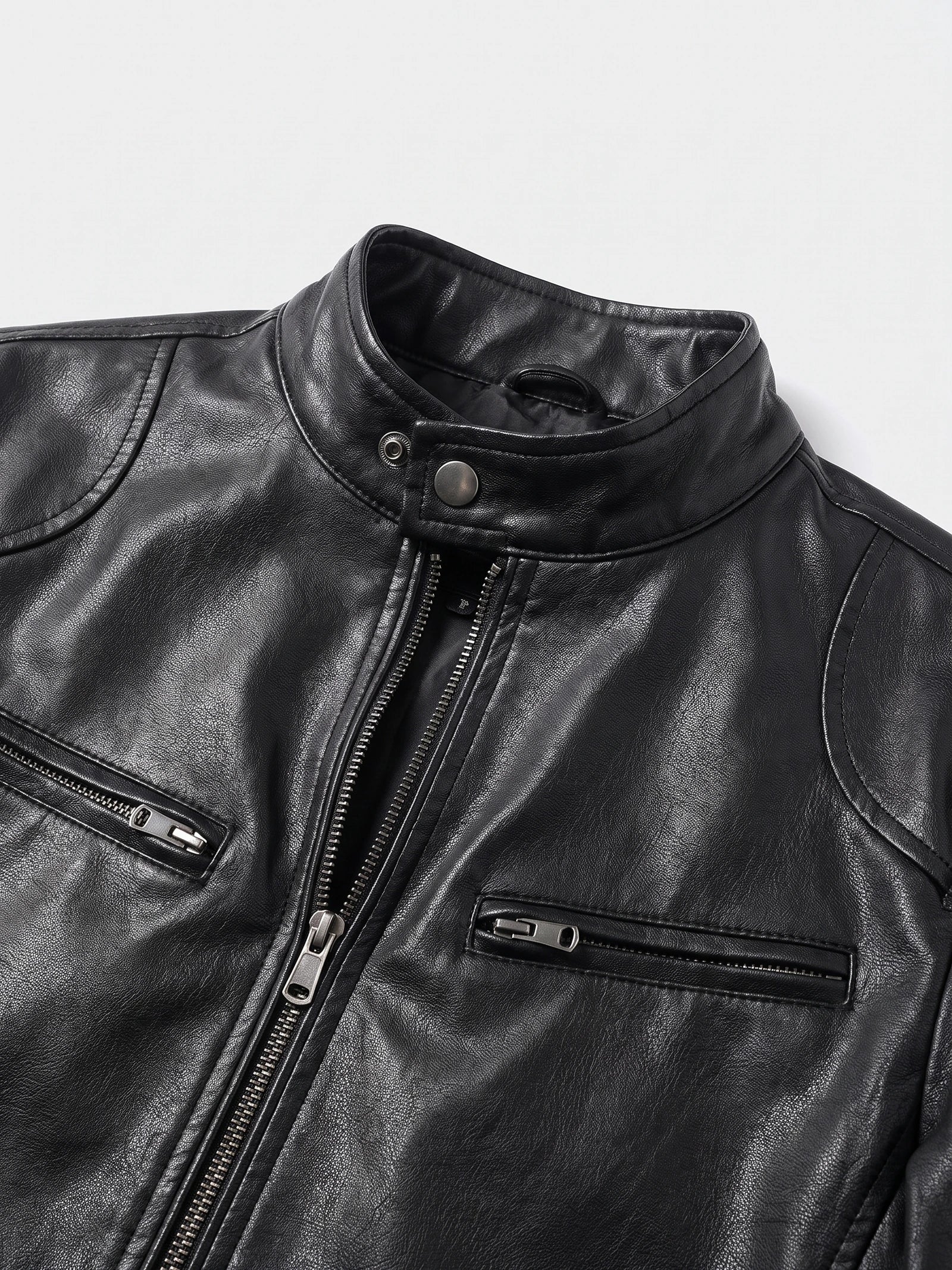 Close-up of a Black men's leather jacket with a snap-tab stand collar, front zipper, and zippered chest pockets.