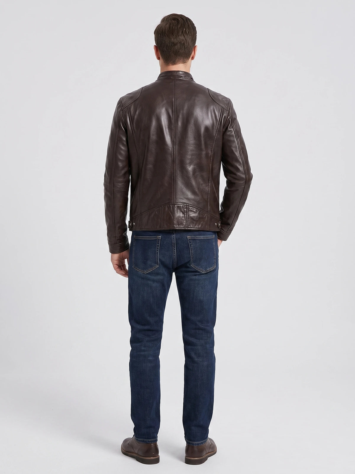 Rear studio view of a model wearing a Brown men's leather jacket with a center back seam and adjustable waist tabs.