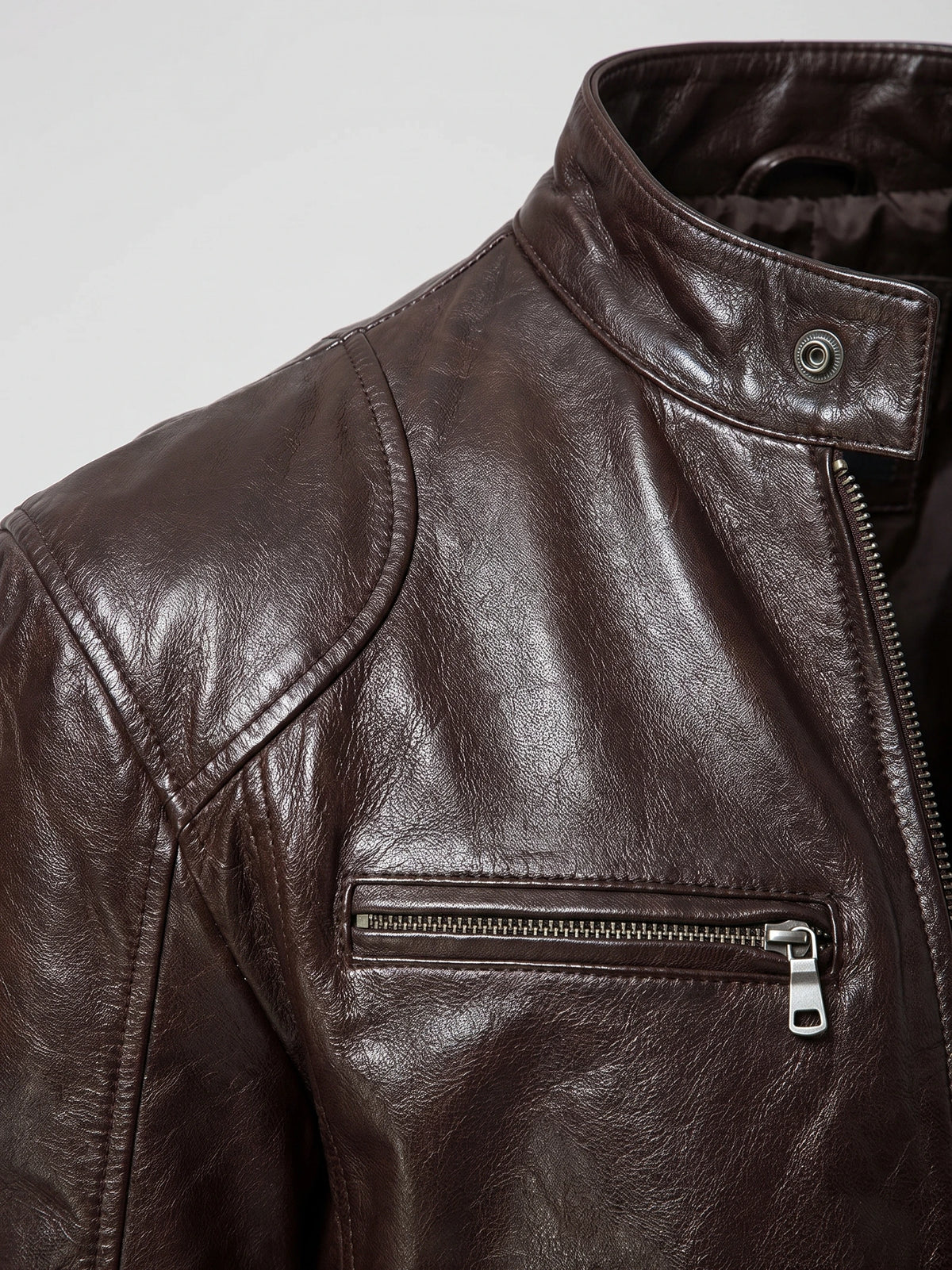 Close-up of a Brown men's leather jacket with a snap-tab collar, shoulder stitching, and zippered chest pocket.