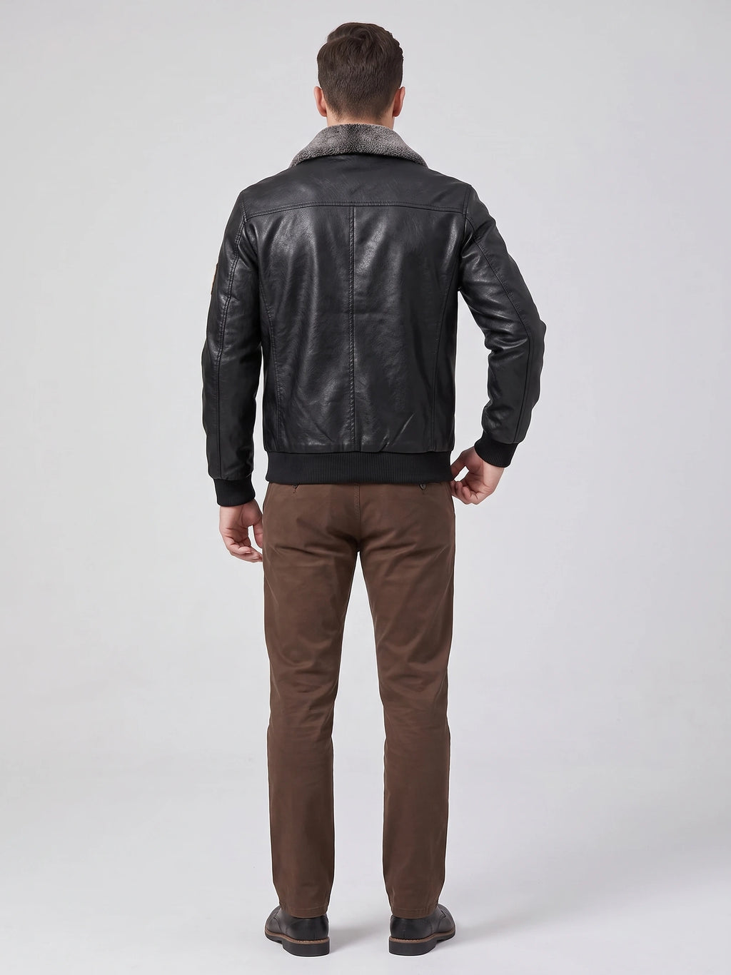Back view of a model wearing a Black Leather Jacket with a textured fur collar, ribbed hem and cuffs, and vertical back seam detailing.