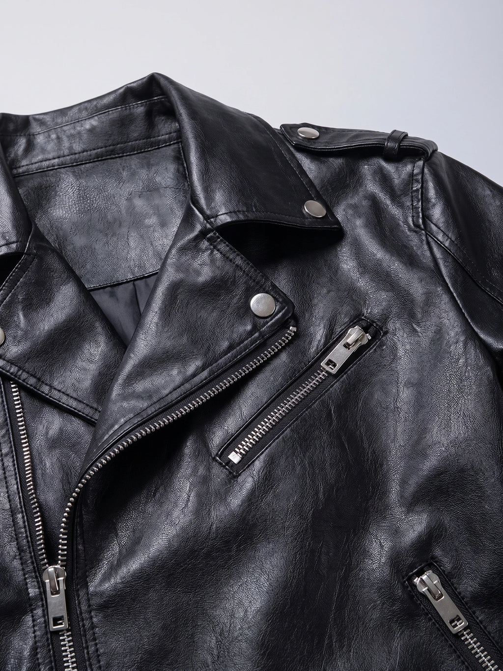 Close-up of a Black PU leather motorcycle jacket with a snap lapel, shoulder tab, and zippered chest pockets.