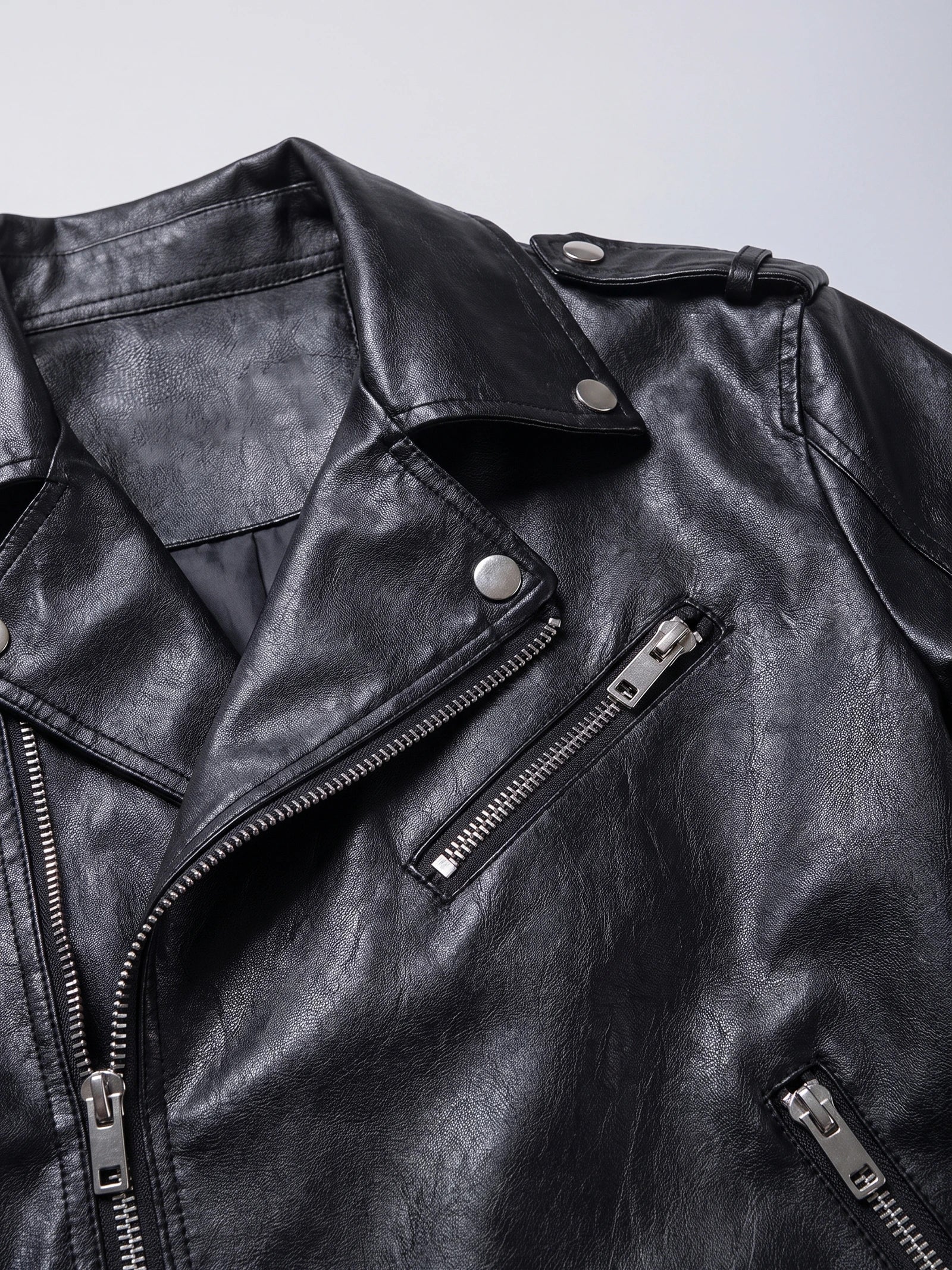 Close-up of a Black PU leather motorcycle jacket with a snap lapel, shoulder tab, and zippered chest pockets.