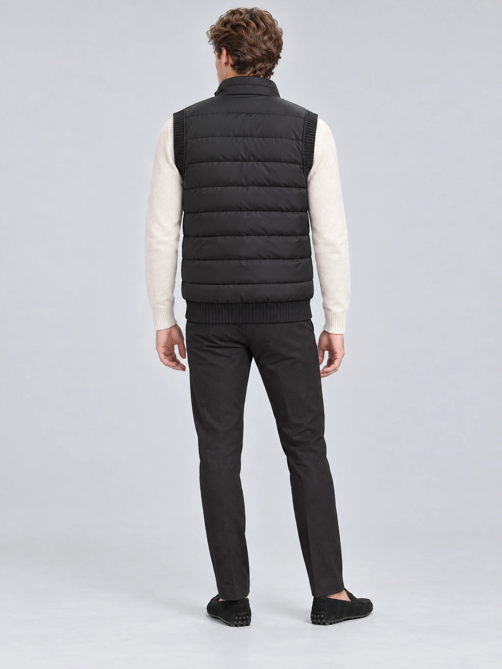 Rear view of a model wearing a Black lightweight puffer vest with horizontal quilting, ribbed trim, and a stand collar.
