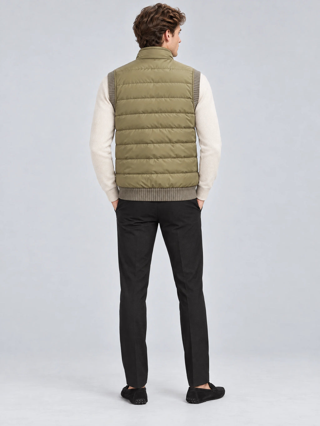 Rear studio view of a model wearing a Khaki lightweight puffer vest with horizontal quilted padding and a stand collar.