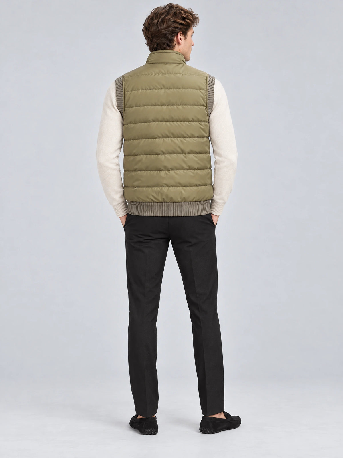 Rear studio view of a model wearing a Khaki lightweight puffer vest with horizontal quilted padding and a stand collar.