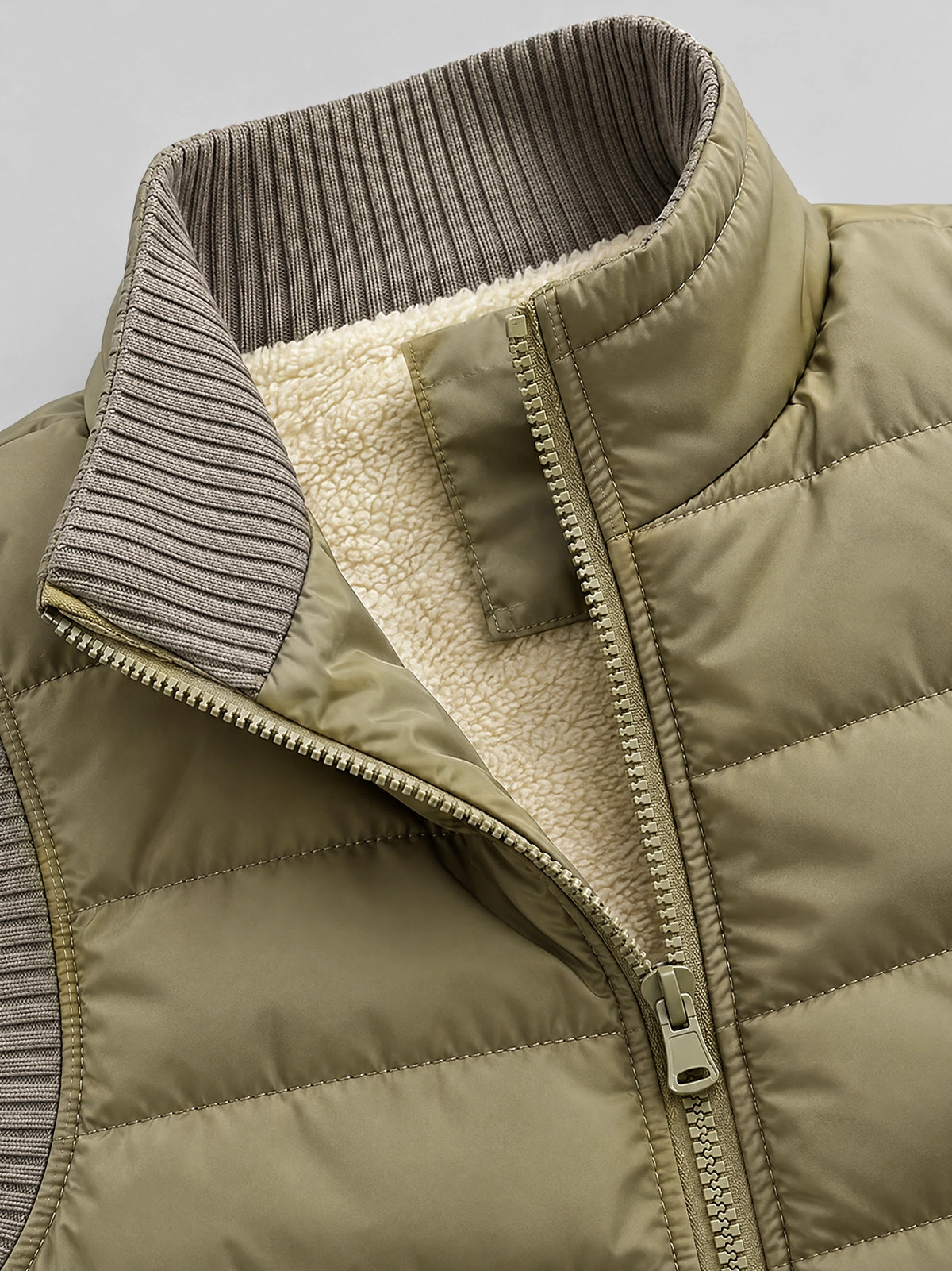 Khaki lightweight puffer vest close-up showing the ribbed collar, front zipper, quilted stitching, and soft inner lining.