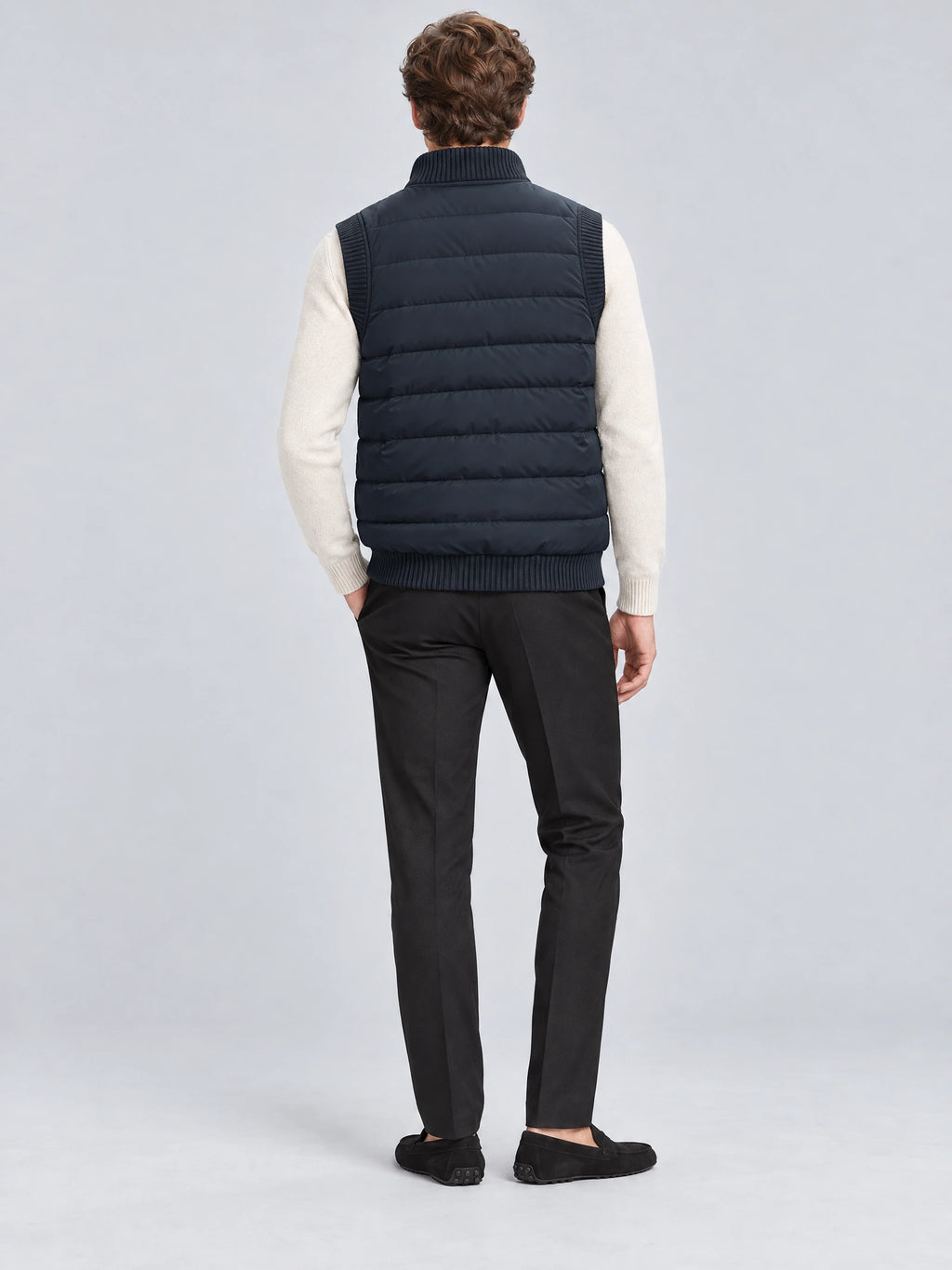 Rear studio view of a model wearing a Navy lightweight puffer vest with horizontal quilting and ribbed collar and hem.