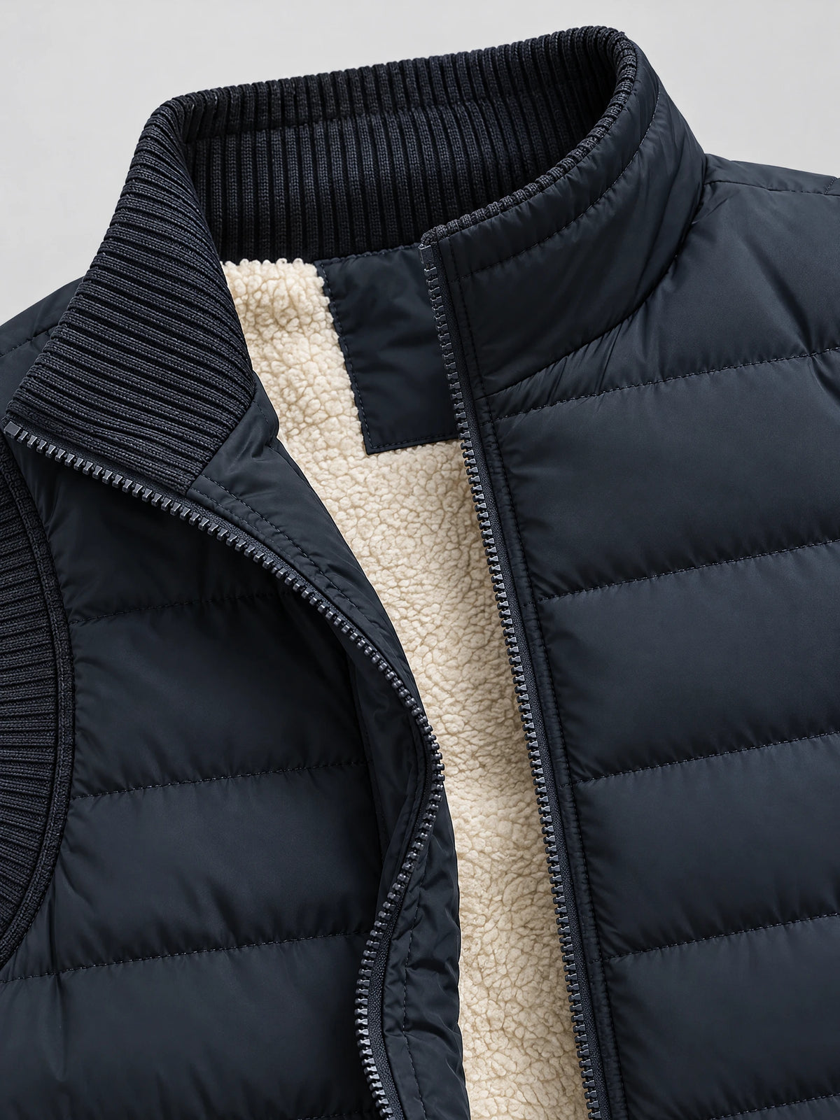Navy lightweight puffer vest detail showing the ribbed stand collar, front zipper, quilted shell, and textured lining.