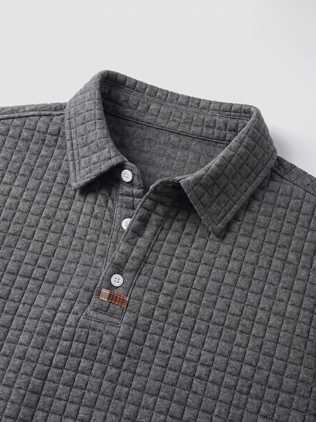 Gray cotton long sleeve polo close-up showing the textured knit collar, three-button placket, and stitched accent tab.
