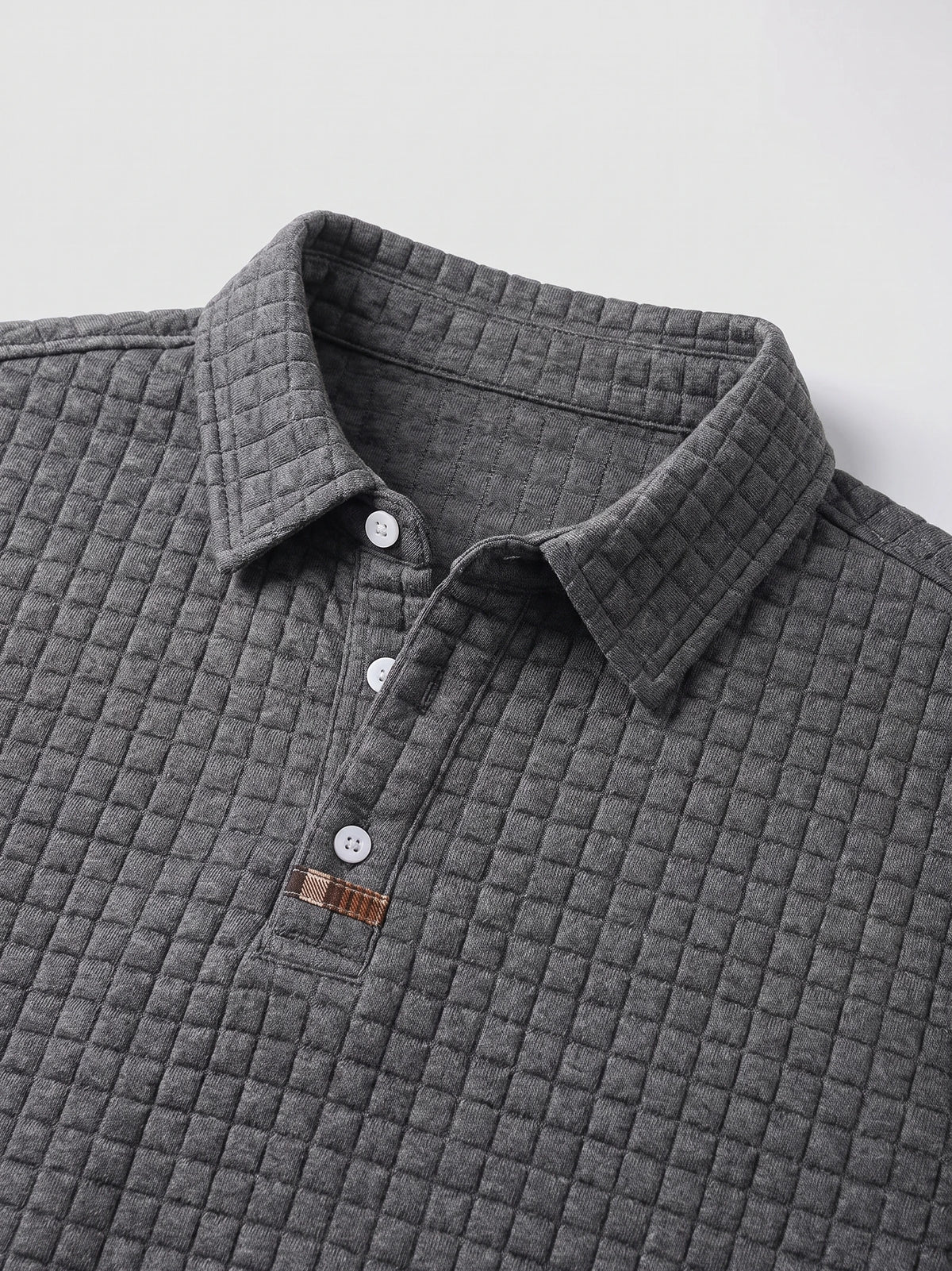Gray cotton long sleeve polo close-up showing the textured knit collar, three-button placket, and stitched accent tab.