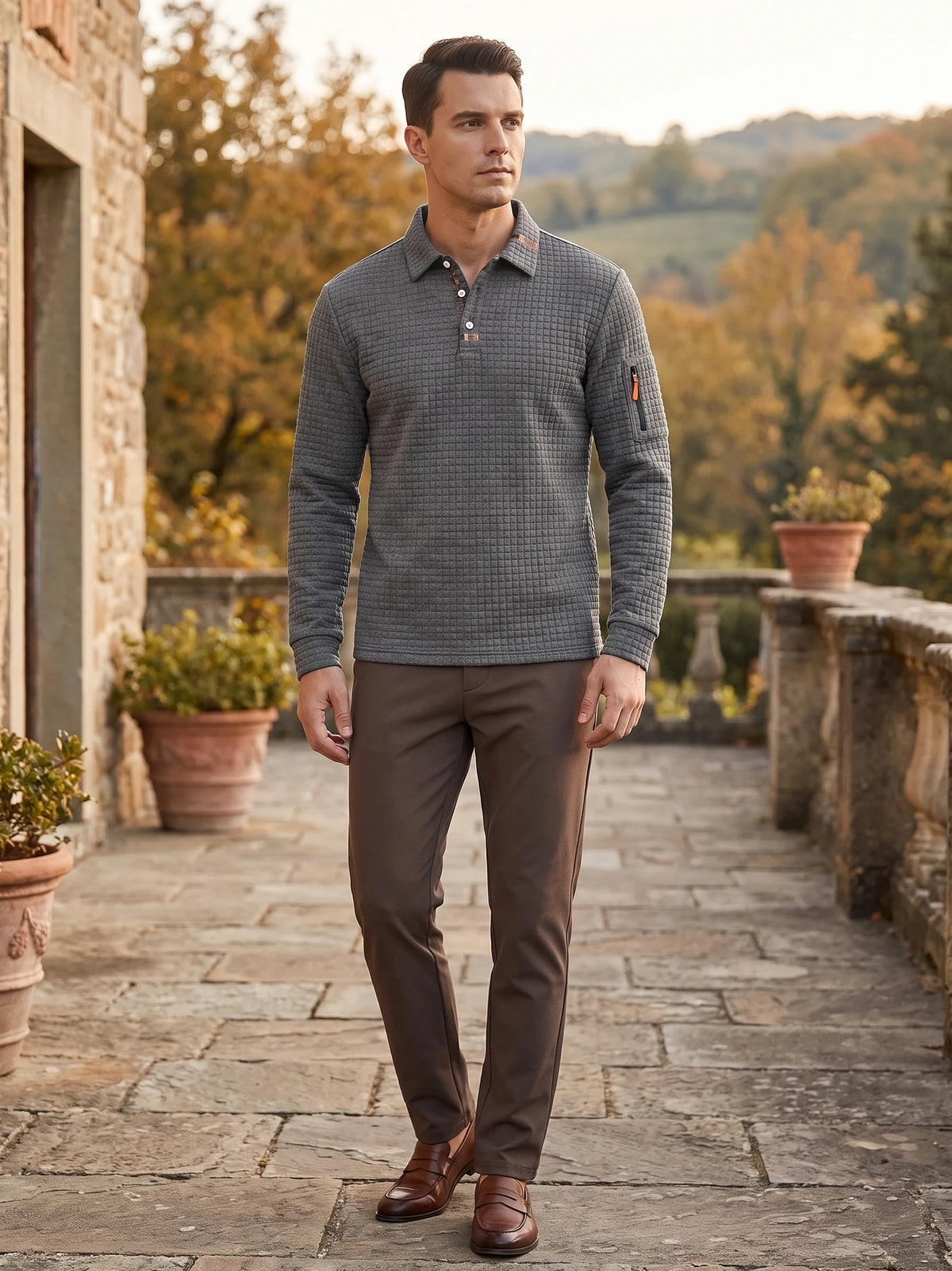 Man wearing a Gray long sleeve polo with textured fabric and a sleeve zip pocket on a stone terrace.