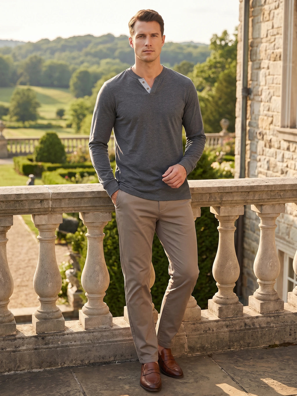 Man wearing a Gray long sleeve Henley shirt on a stone terrace overlooking a landscaped garden.