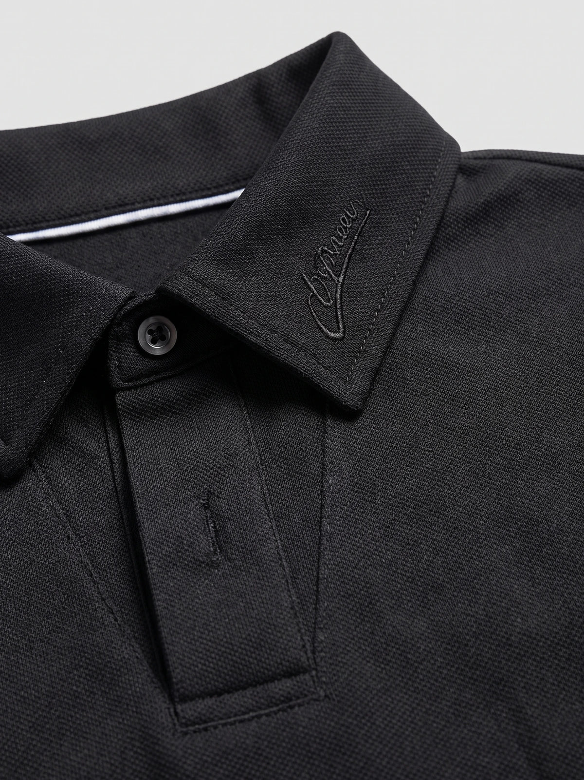 Close-up of the Black Long Sleeve Polo collar, showing tonal embroidery, textured fabric, and button placket.