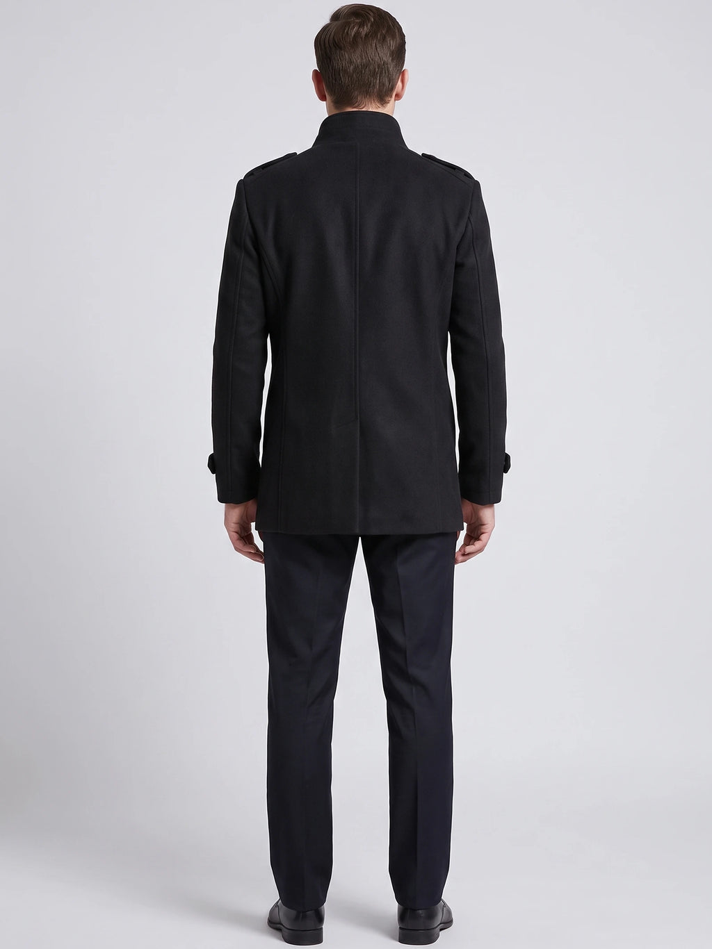 Rear studio view of a model wearing a Black wool overcoat with a stand collar, shoulder tabs, and center back seam.