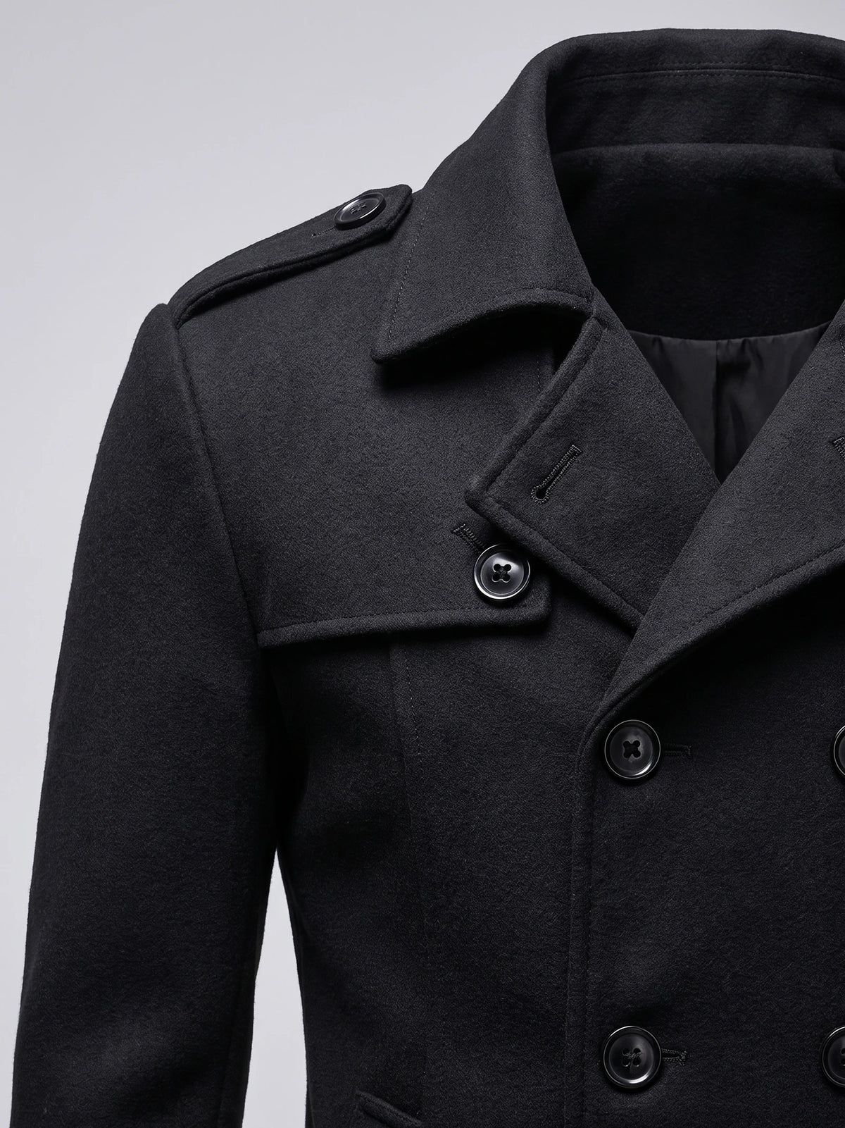 Close-up of a Black wool overcoat with a wide collar, shoulder epaulette, and double-breasted button fastening.